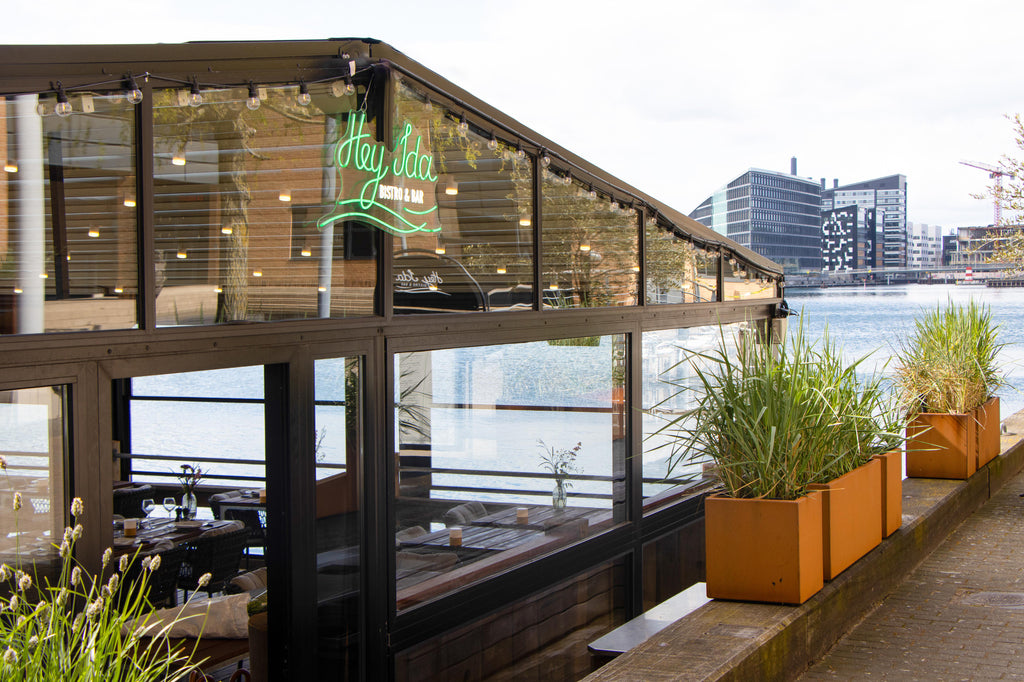 Hey IDA lunch restaurant placed on the water at Kalvebod Brygge in Copenhagen, characteristic green neon sign of Hey IDA, cobber planters with high grass plants 