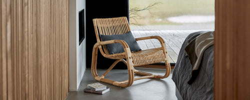 Geflochtene Stuhl mit einem bequemen Kissen, neben einem Bett positioniert, das ein modernes und stilvolles Design in einer ruhigen Umgebung zeigt.