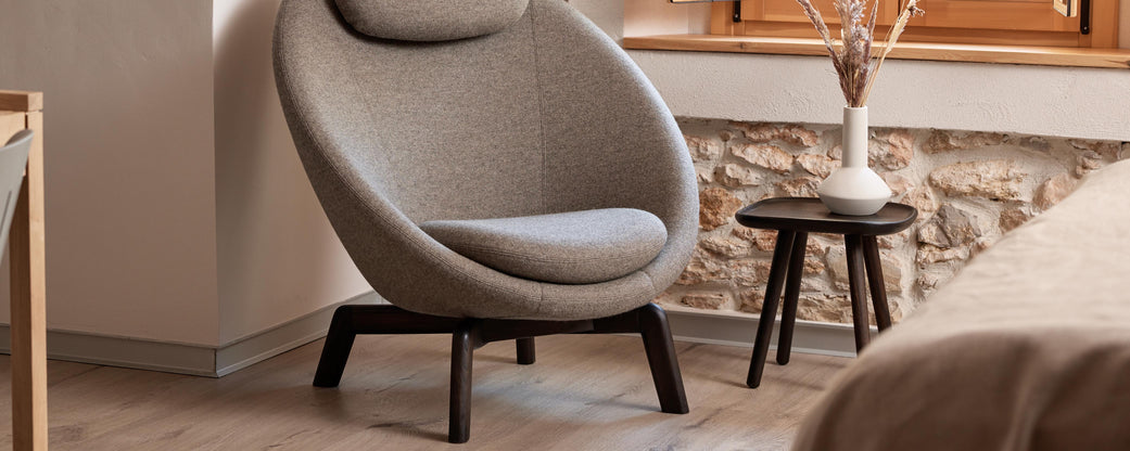 Ein gemütlicher, moderner Sessel, ergänzt durch einen eleganten Beistelltisch, akzentuiert mit einer Vase und dekorativen Elementen vor einer strukturierten Wand.