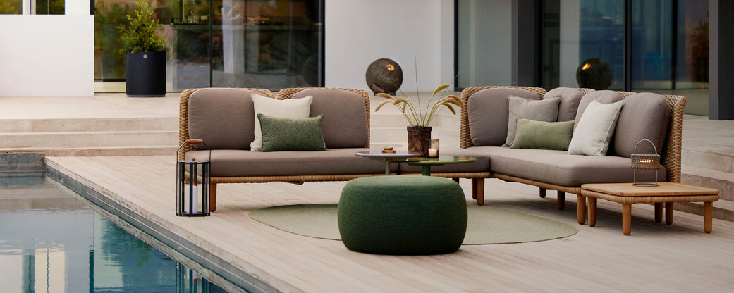 Stylish seating area with soft cushions, a green pouf, and decorative elements, positioned beside a serene pool.