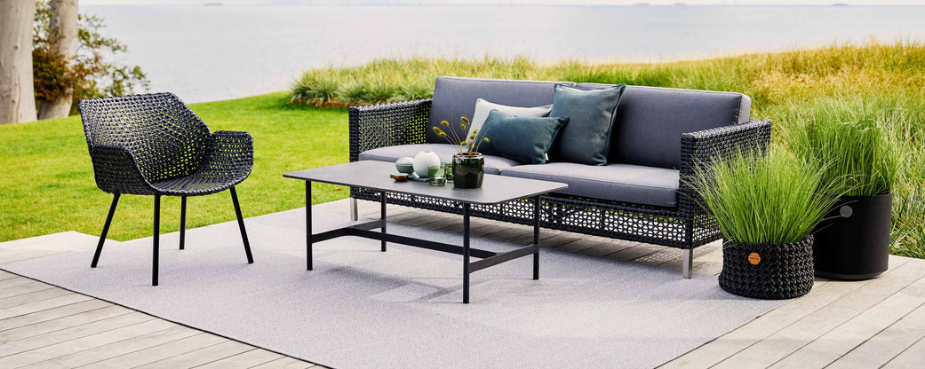 Stylische Sitzanordnung mit einem modernen Sofa, Sessel und Couchtisch, ergänzt durch dekorative Kissen und Pflanzen.