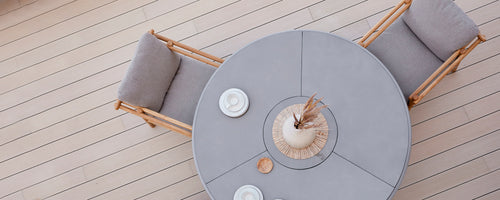 Runder Esstisch mit weichen Sitzgelegenheiten, ergänzt durch dekorative Teller und ein Mittelarrangement. Einfaches, elegantes Design.