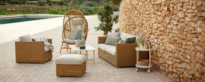 Moderne Outdoor-Lounge-Bereich mit braunem Rattansofa und Stühlen mit beigen Kissen.