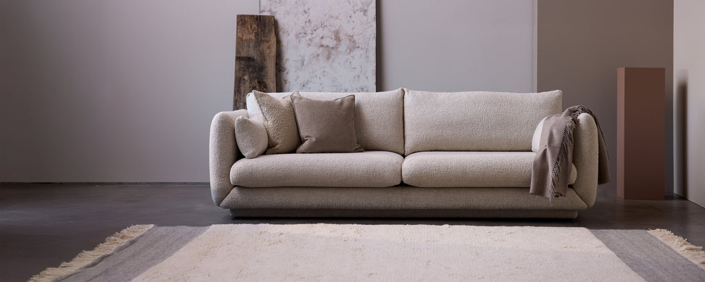 Beige Sofa mit grauen Kissen in einer modernen Lounge-Umgebung.
