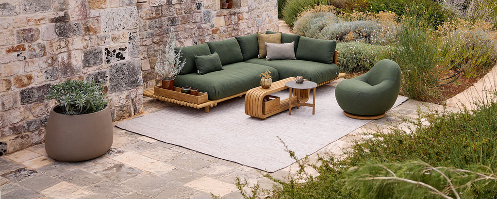 Moderne Outdoor-Lounge-Einstellung mit grünem Ecksofa, Stuhl, Holztisch und grauem Teppich.