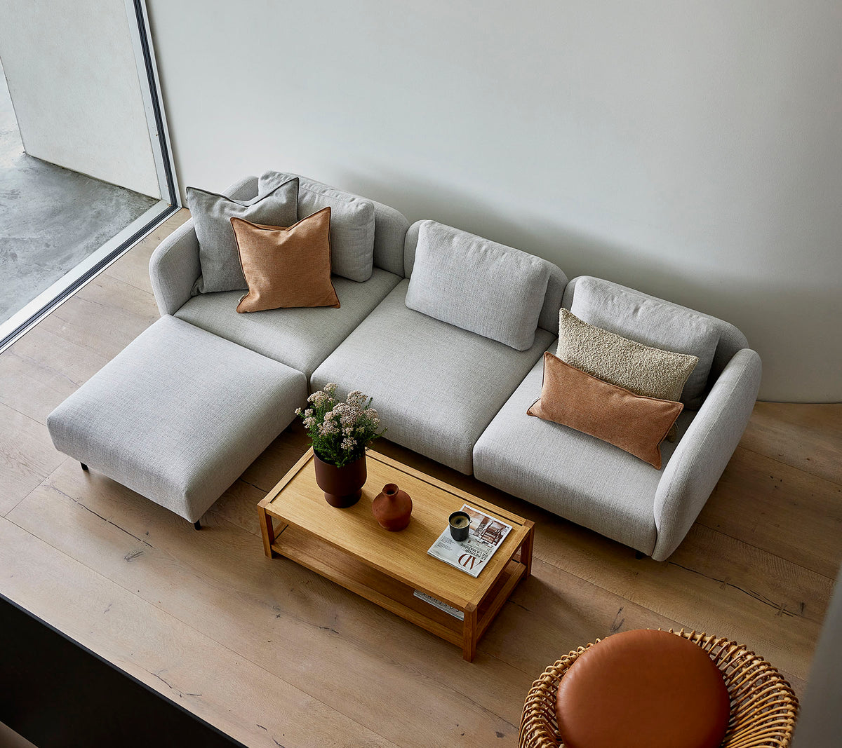 Ein stilvolles hellgraues Ecksofa mit Kissen, kombiniert mit einem Holztisch und einer runden Sitzgelegenheit, die eine gemütliche Atmosphäre schafft.