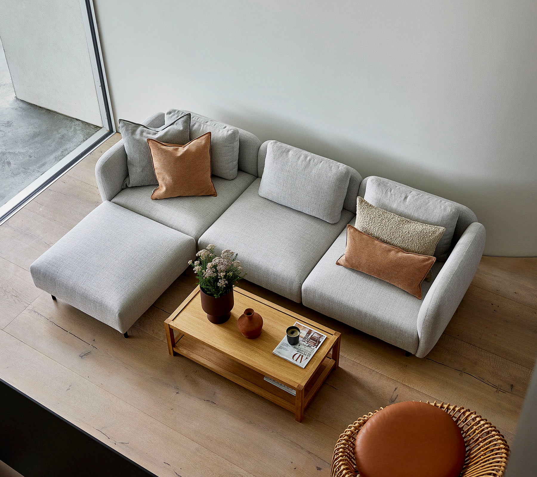 Ein stilvolles hellgraues Ecksofa mit Kissen, kombiniert mit einem Holztisch und einer runden Sitzgelegenheit, die eine gemütliche Atmosphäre schafft.