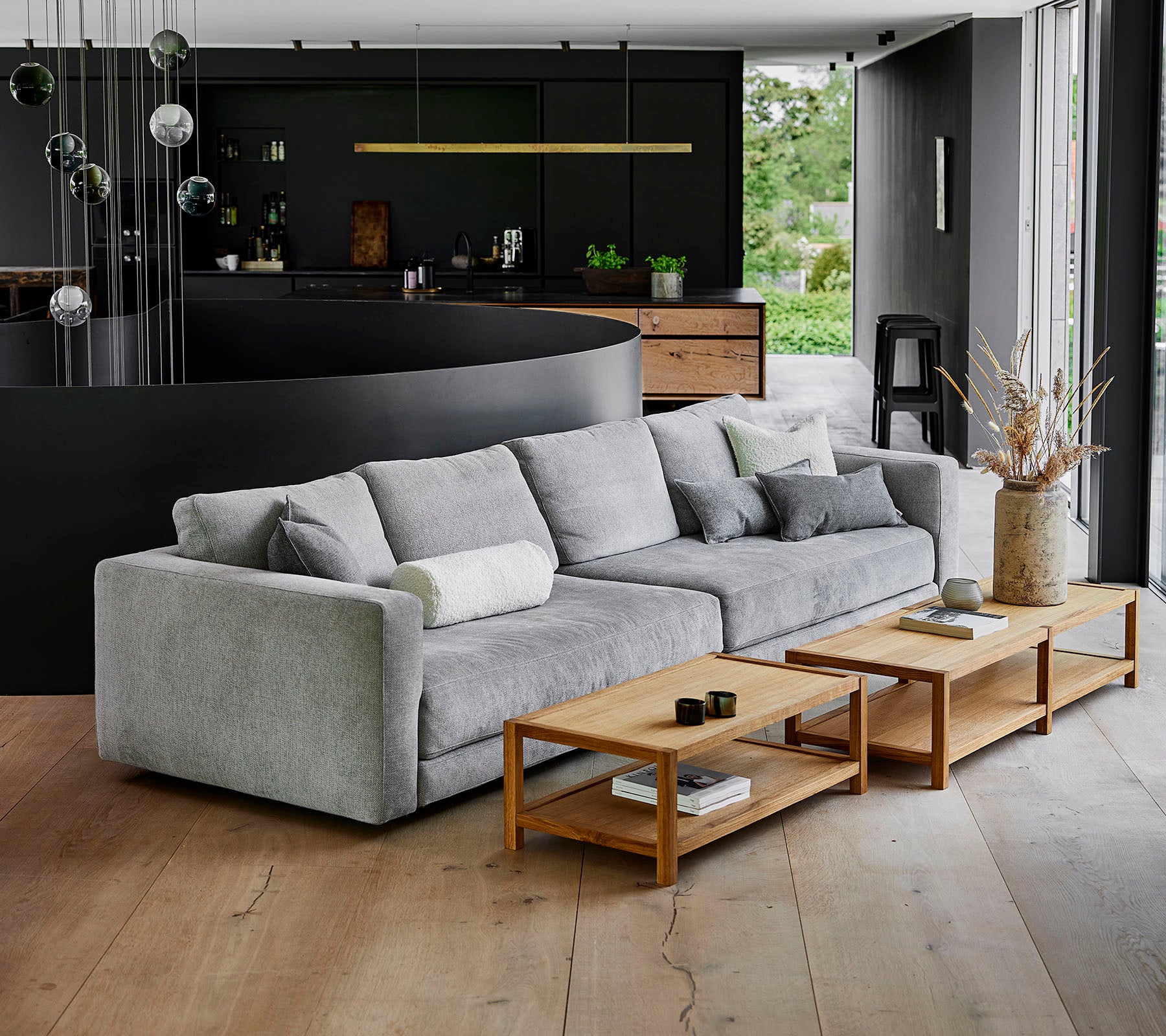 Ein modernes, graues Sofa mit plüschigen Kissen neben Holztischen in einer zeitgemäßen Umgebung mit stilvoller Dekoration.