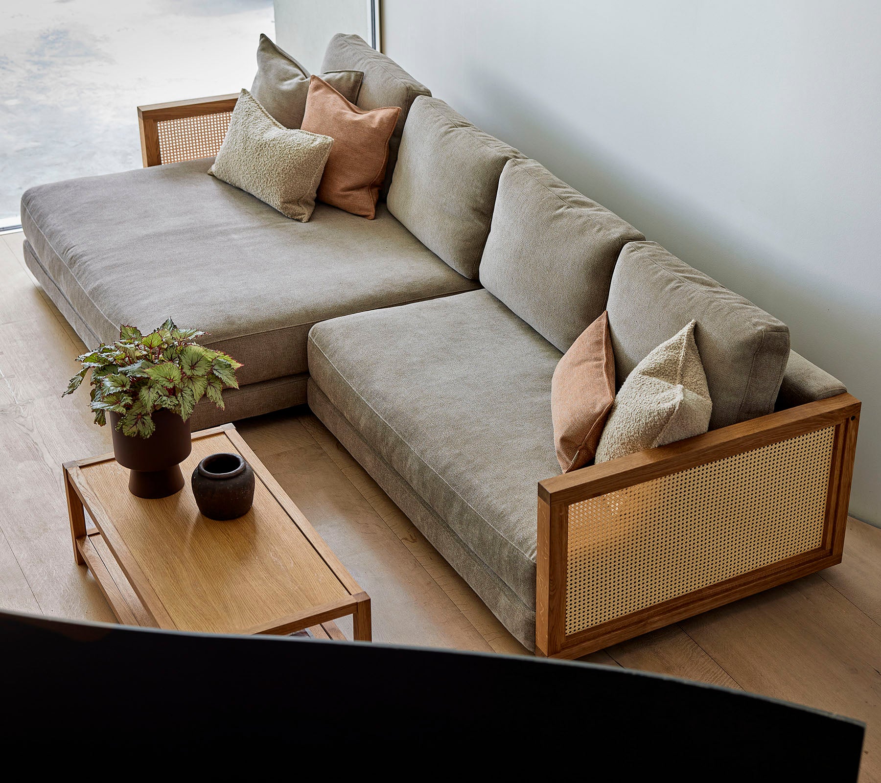Ein stilvolles Ecksofa mit weichen Kissen und dekorativen Kissen, kombiniert mit einem Holztisch, der Pflanzen und elegante Dekoration aufweist.