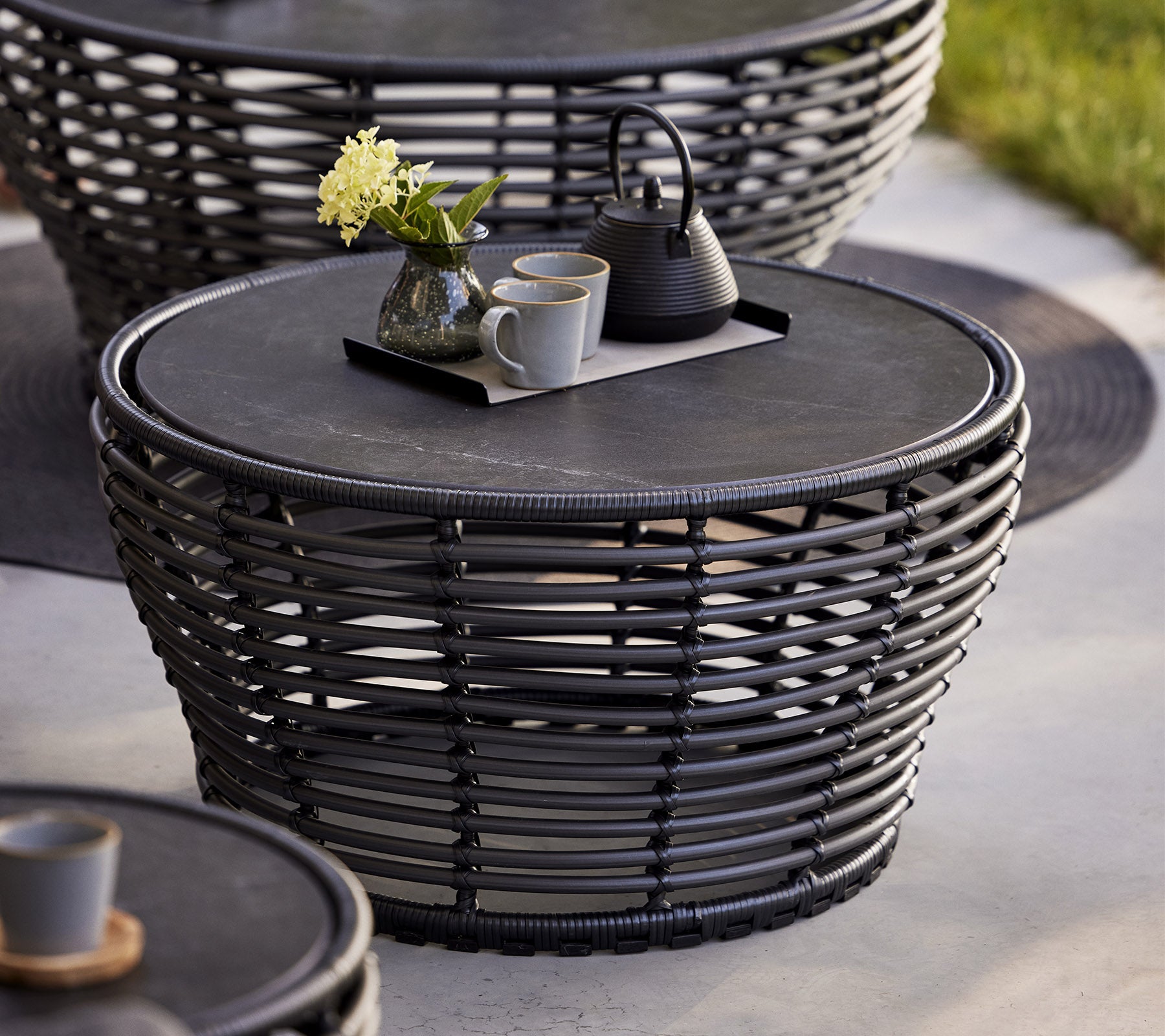 Stilvolles geflochtenes Couchtisch mit einer runden Oberfläche, das mit einem dekorativen Tablett, einer Teekanne und Tassen sowie einer Blumenvase ergänzt wird.