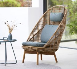 Stylischer geflochtener Stuhl mit hoher Rückenlehne, gepolsterter Sitzfläche und passendem Kissen, begleitet von einem kleinen Tisch und einer dekorativen Vase.
