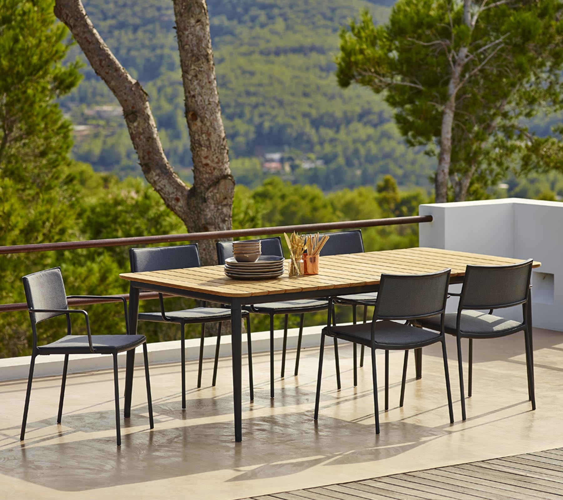 Esstischset für den Außenbereich mit einer rechteckigen Holzoberfläche und schwarzen Stühlen, umgeben von Grün und malerischen Aussichten.