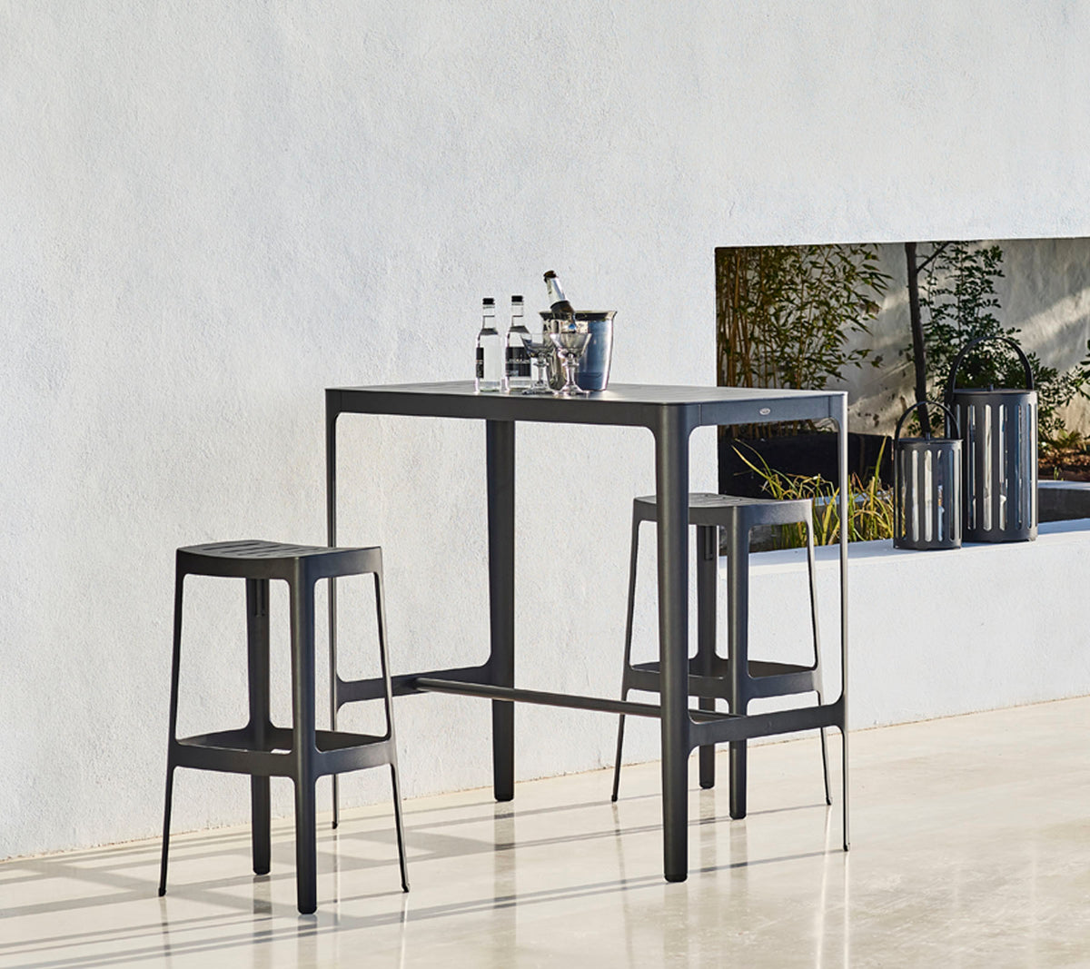 Ein eleganter Tisch mit zwei passenden Hockern, der ein minimalistisches Design aufweist und Flaschen oben darauf platziert sind, vor einem neutralen Hintergrund.