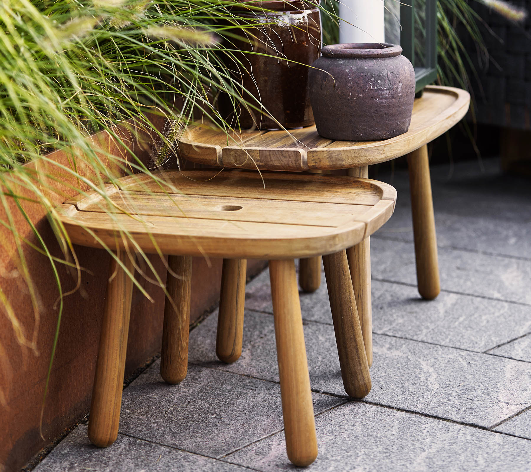 Zwei stilvolle Holzhocker in unterschiedlichen Höhen, ergänzt durch einen keramischen Topf und Pflanzen im Hintergrund. Ideal für dekorative Zwecke.