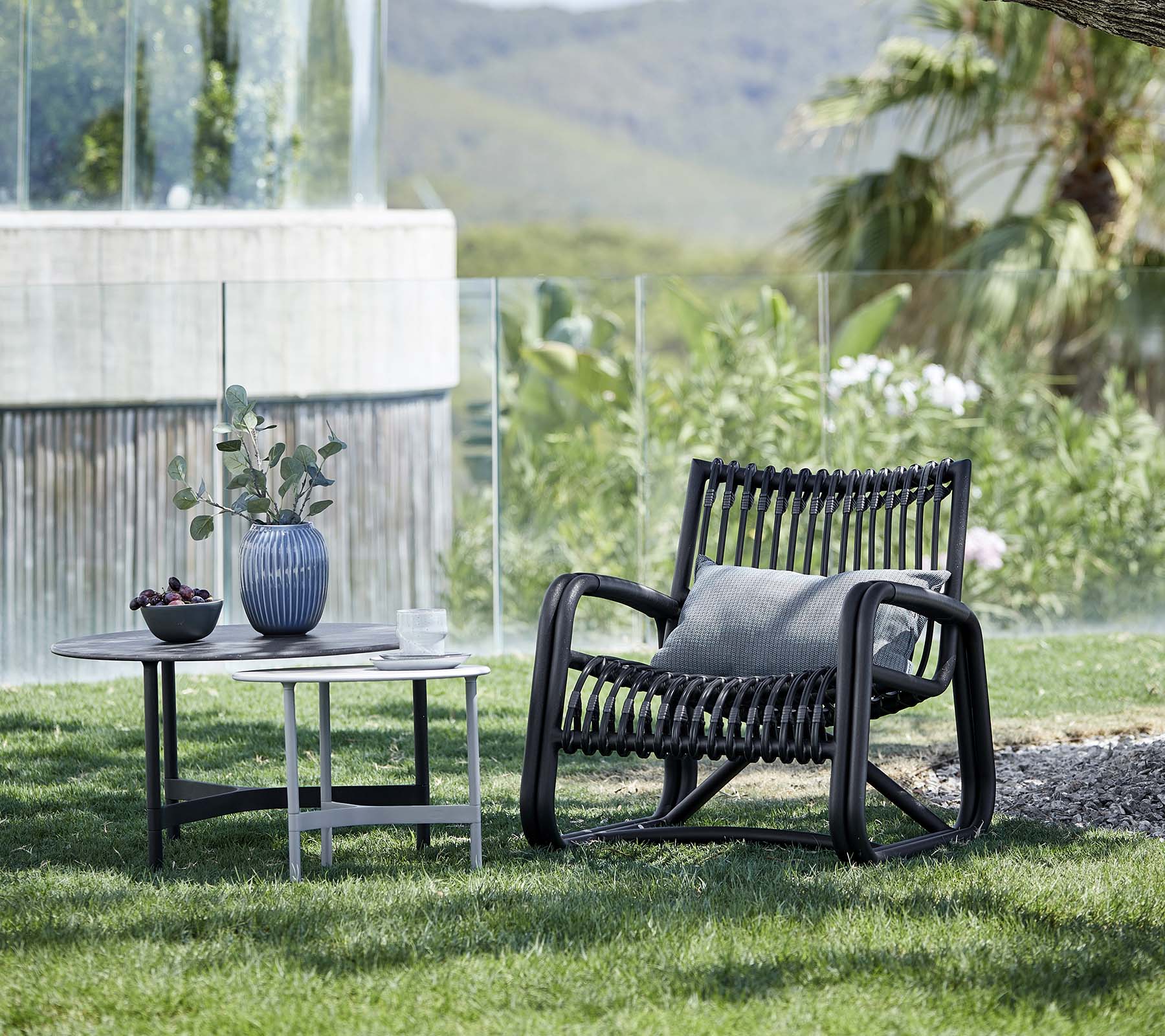 Zeitgenössischer Loungesessel mit einem gemusterten Design, begleitet von einem Beistelltisch mit einer Vase und einer Topfpflanze, in einer natürlichen Landschaft.