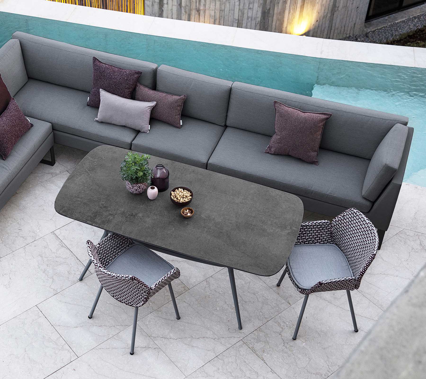 Moderner Außenbereich mit einer modularen Sofa mit Kissen, einem eleganten rechteckigen Tisch und stilvollen Stühlen, ergänzt durch einen Blick auf den Pool.