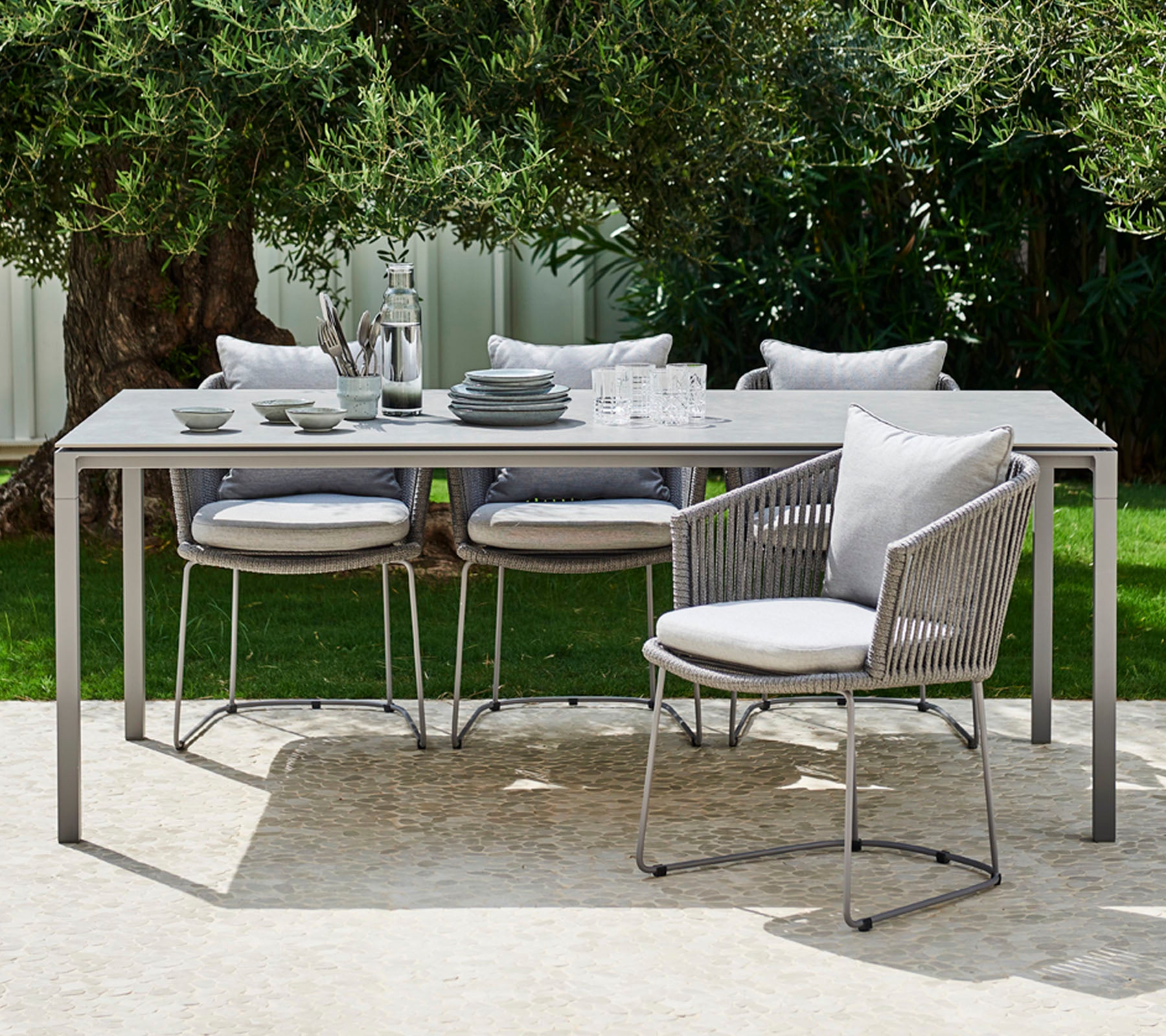 Ein modernes Outdoor-Esszimmer-Set mit einem schlanken Tisch, gepolsterten Stühlen und elegantem Geschirr, das für eine stilvolle Mahlzeit angerichtet ist.