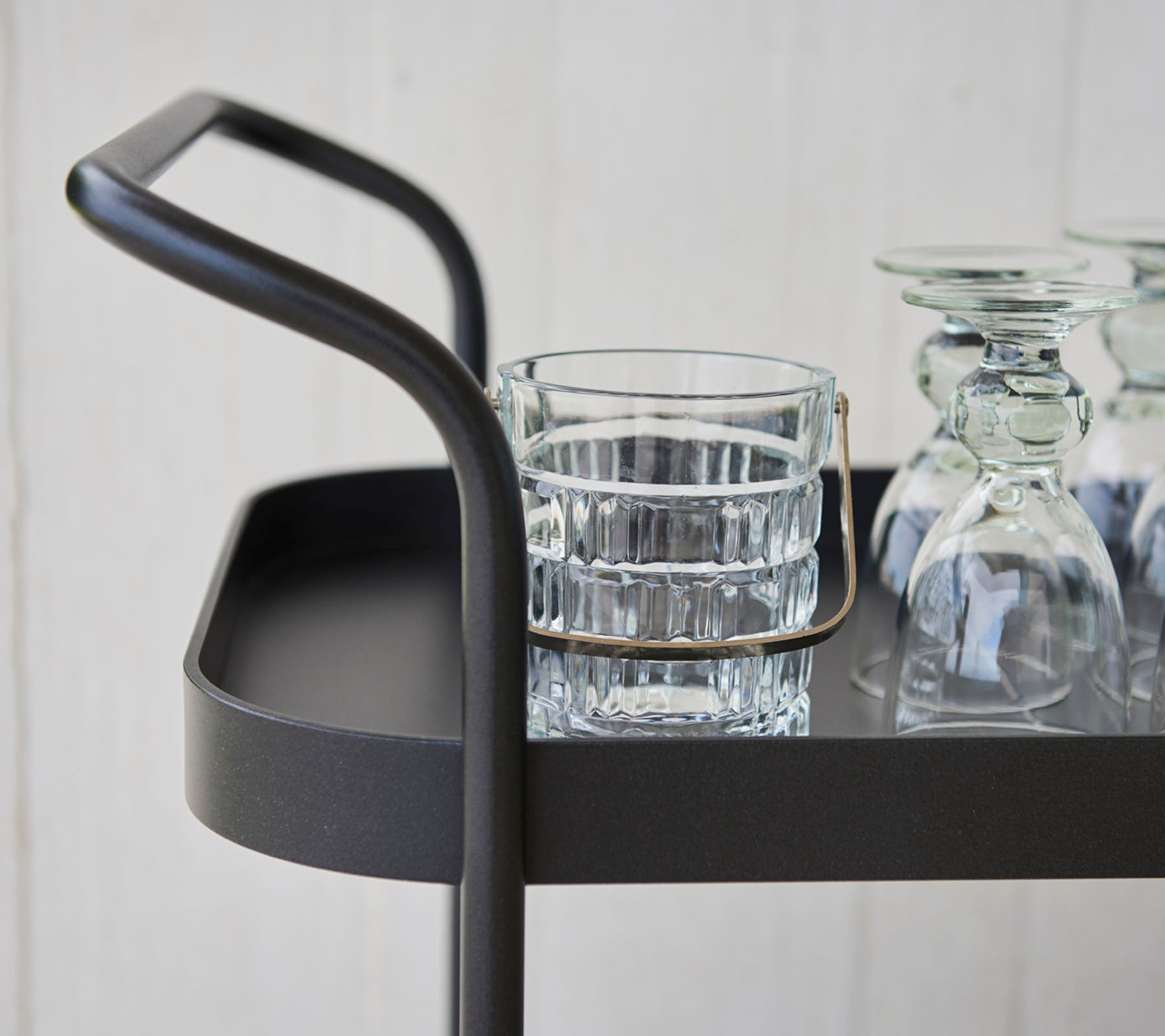 Stilvoller Servierwagen mit einem schlanken Griff, ausgestattet mit einem Glastumbler und mehreren klaren Glaswaren auf einer flachen Oberfläche.