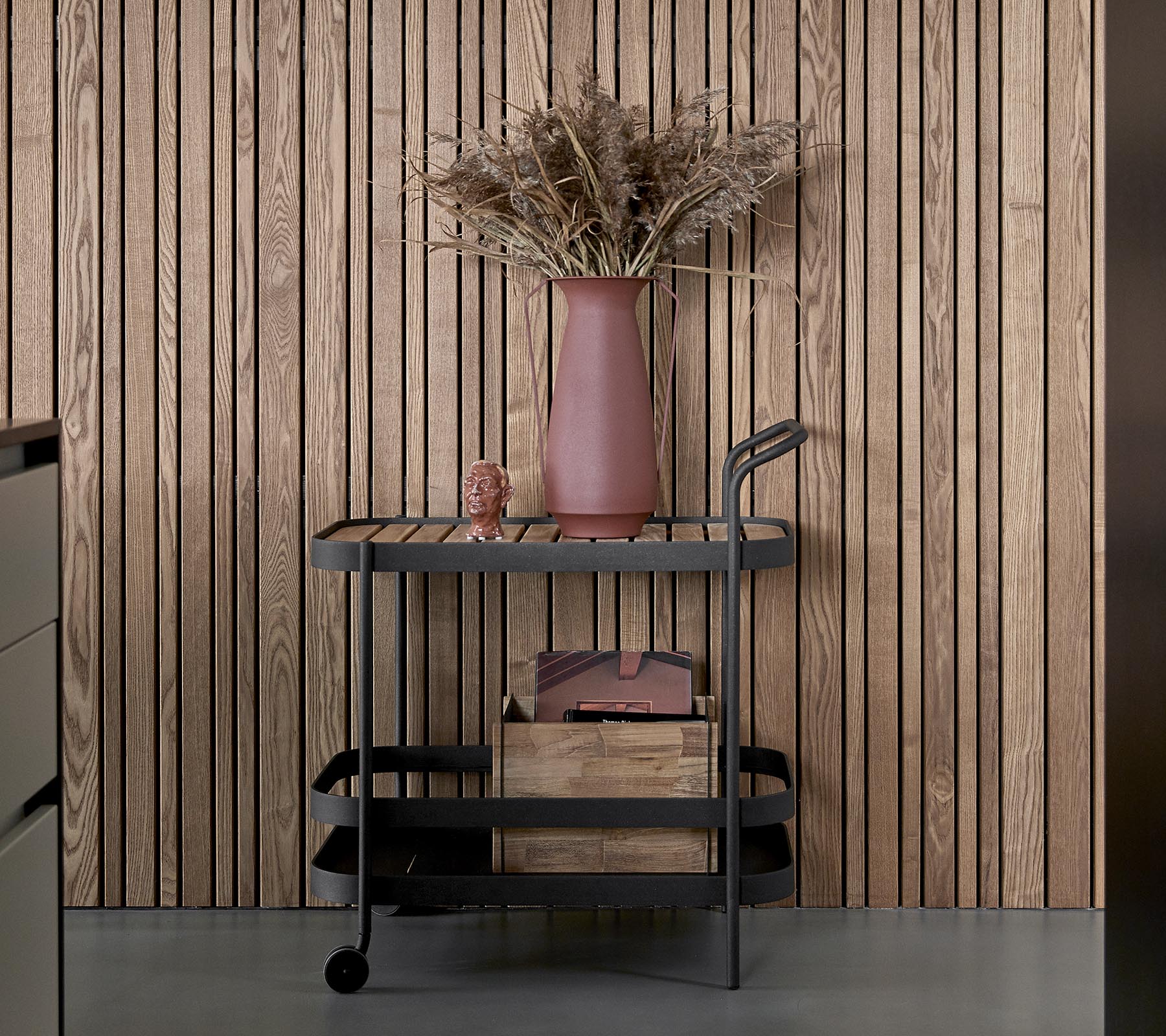 Ein eleganter Wagen mit dunkler Oberflächenbeschaffenheit, ausgestattet mit Holzaufbewahrungsboxen und einer rosa Vase mit getrockneten Blumen.