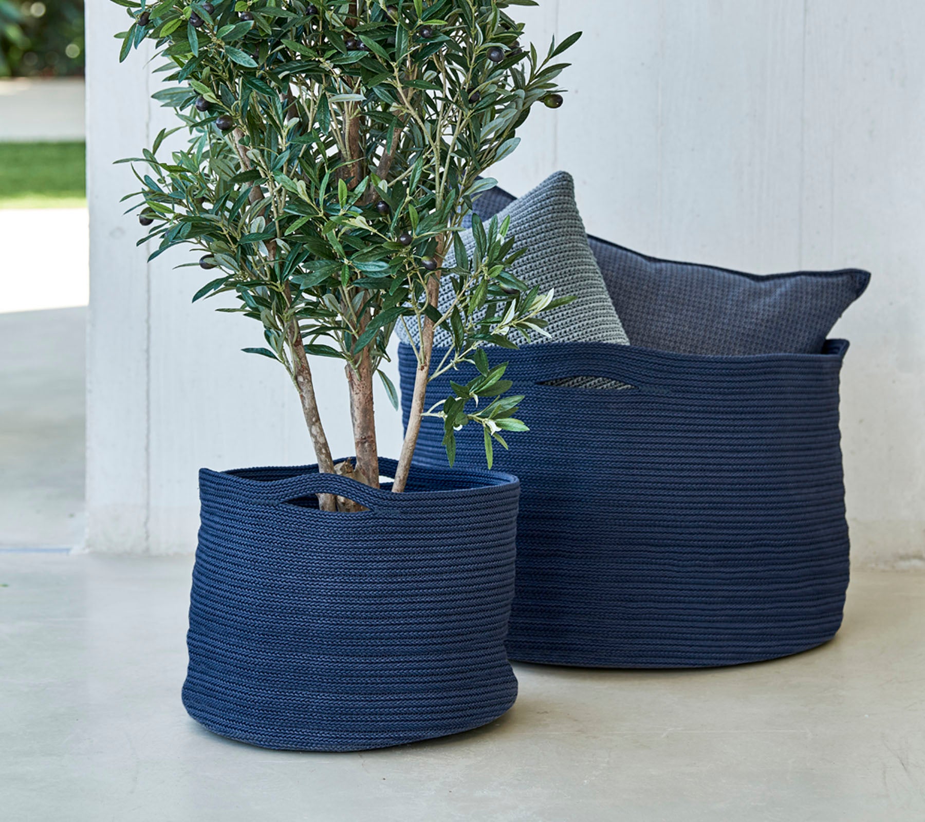Zwei marineblaue gewebte Blumenkübel, einer mit einem kleinen Baum, begleitet von einem dekorativen Kissen.