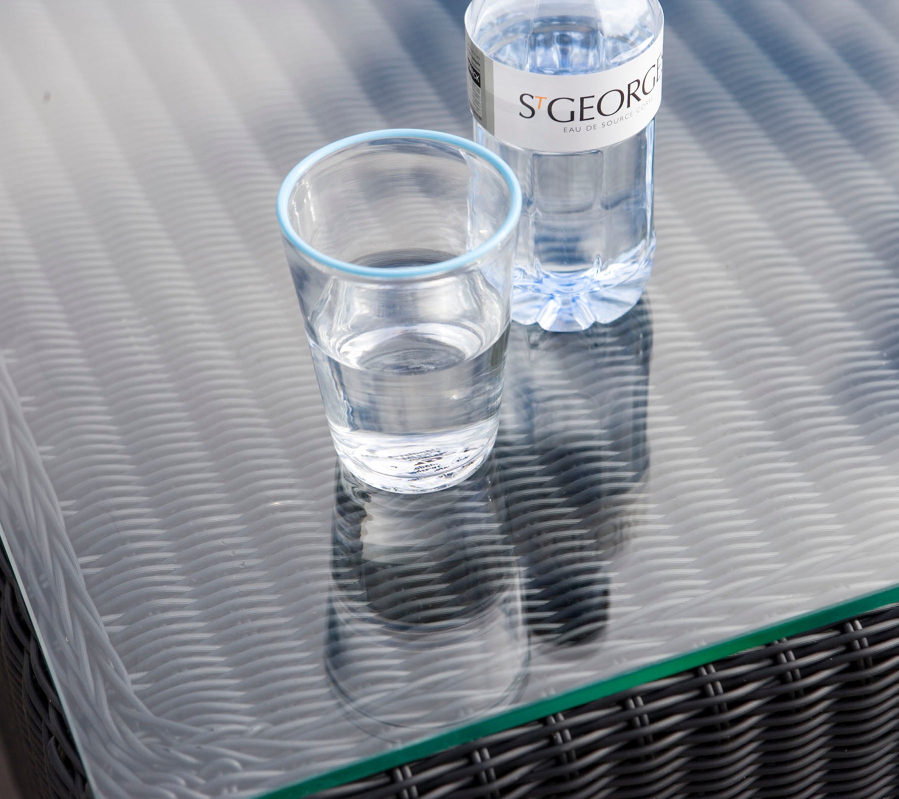 Ein klares Glas mit Wasser neben einer Wasserflasche auf einer strukturierten Tischoberfläche.