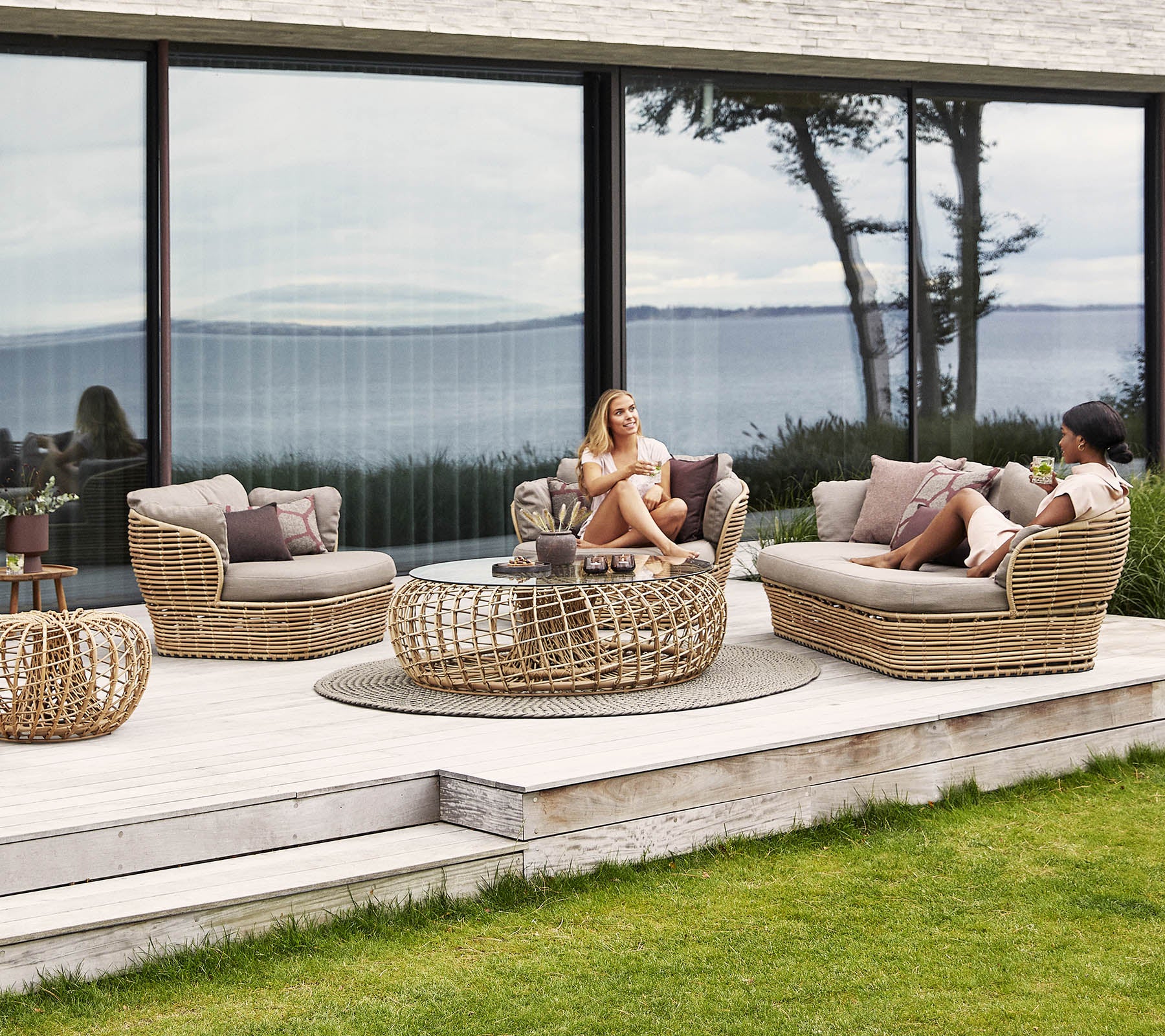 Ein stilvolles Rattan-Sitzbereich mit Kissen, ausgestattet mit einem Kaffeetisch und ruhigen Ausblicken im Hintergrund, ideal zum Entspannen.
