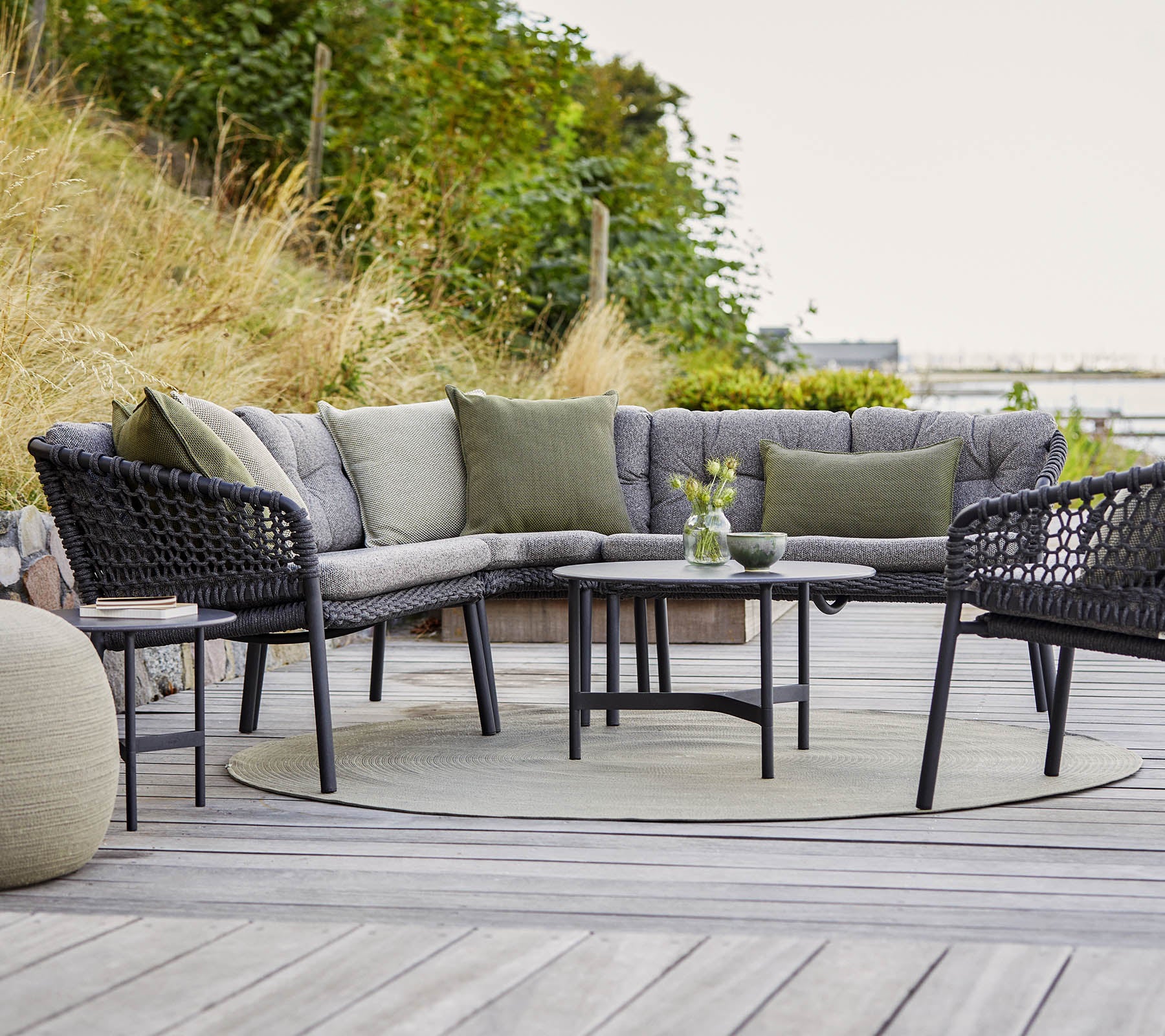 Stylische Sitzgelegenheit im Freien mit einem geschwungenen sectional Sofa, rundem Tisch und gemütlichen Akzenten in einer natürlichen Umgebung.