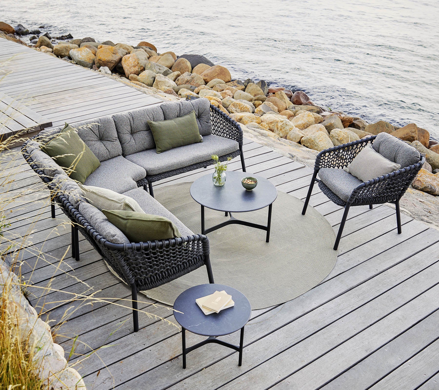 Eine stilvolle Outdoor-Sitzgruppe mit einer modularen Couch und Stühlen mit grauen Kissen, einem runden Tisch und dekorativen Akzenten.