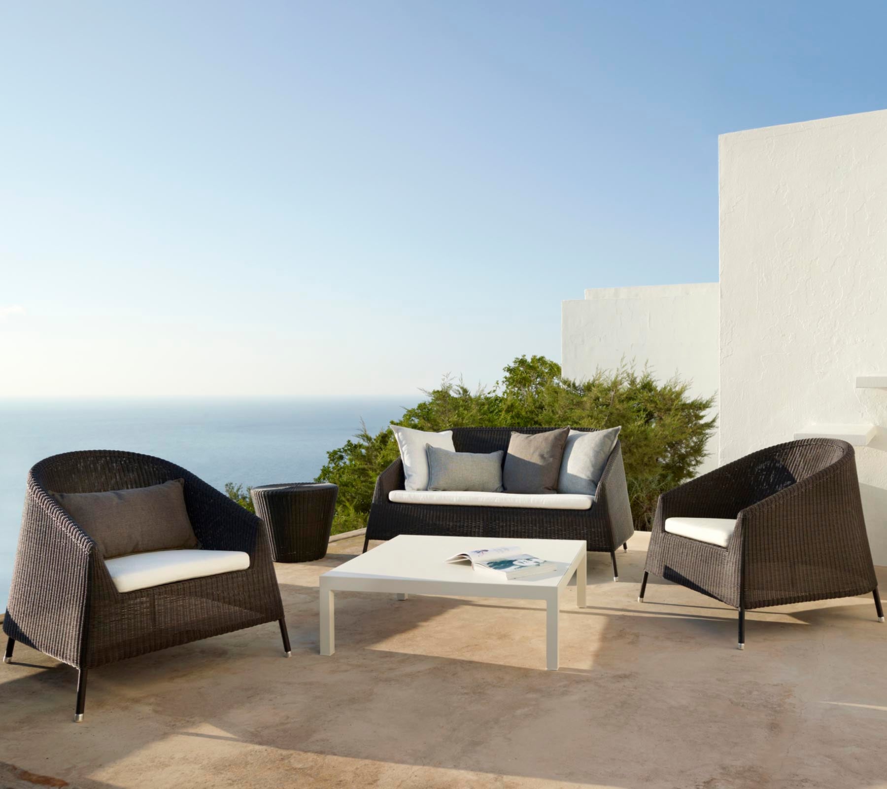 Stilvolles Outdoor-Sitzarrangement mit einem Sofa und Stühlen mit Kissen, ergänzt durch einen Glastisch, ideal zum Entspannen.