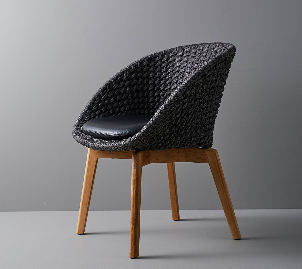 Stilvoller, gewebter Stuhl mit einem bequemen Kissen, ausgestattet mit glatten, konischen Holzbeinen und einem modernen Design, das für verschiedene Umgebungen geeignet ist.