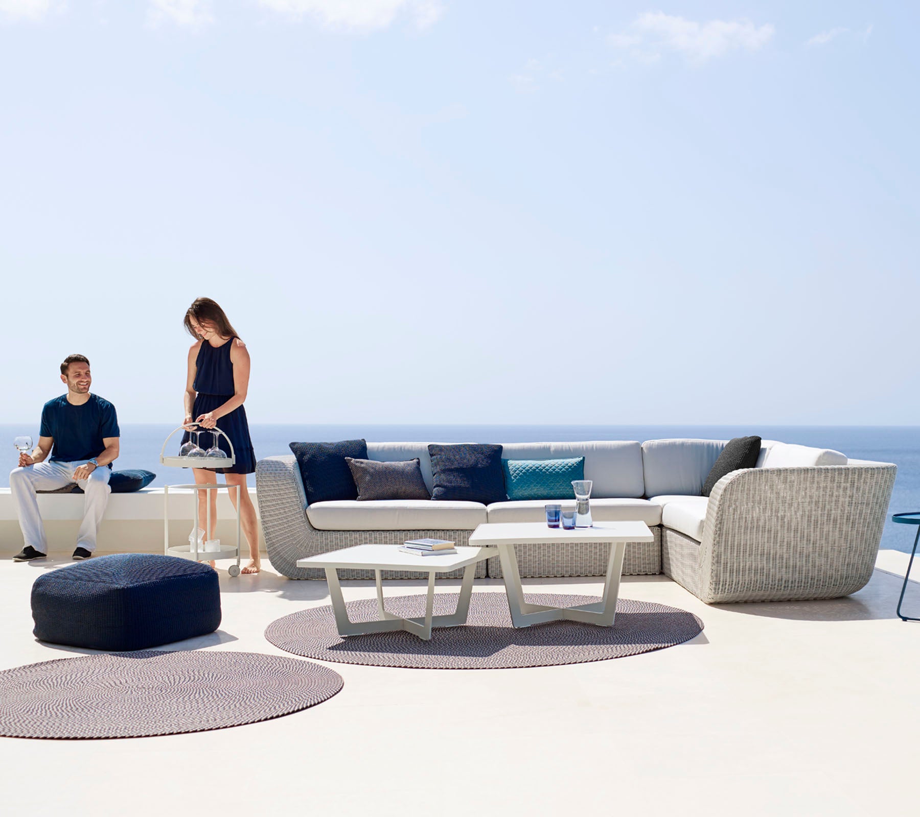 Ein modernes Außenbereich mit einer modularen Sofa, einem Couchtisch und dekorativen Teppichen, wo zwei Personen den Raum genießen.