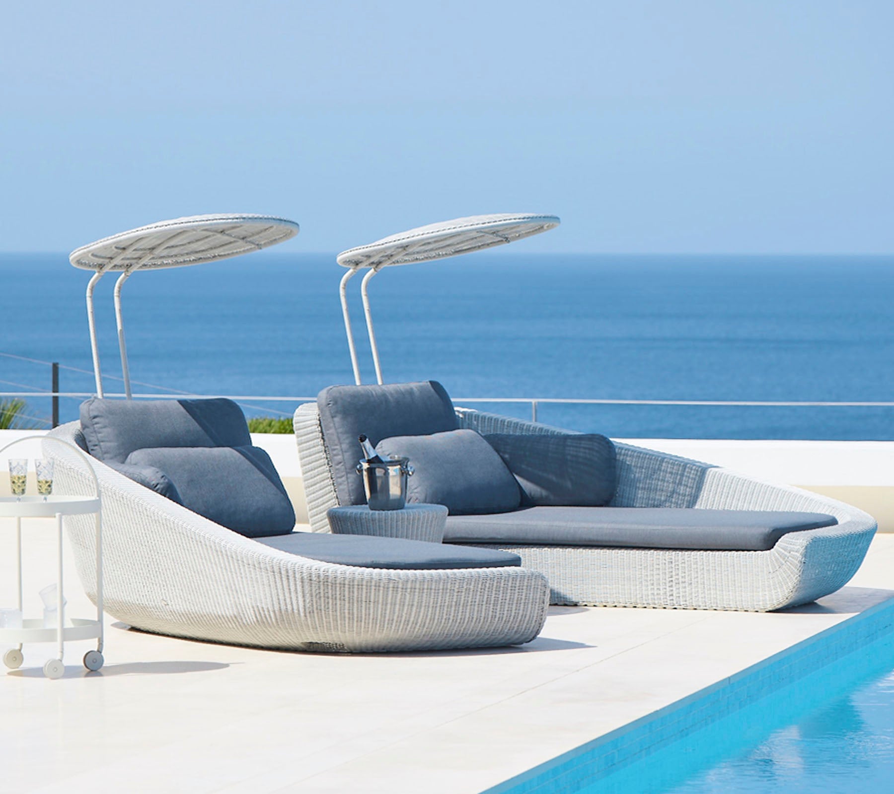 Stylische Loungesessel im Freien mit Sonnendächern neben einem ruhigen Pool, mit Blick auf ein ruhiges Meer. Perfekt zum Entspannen und zur Freizeit.