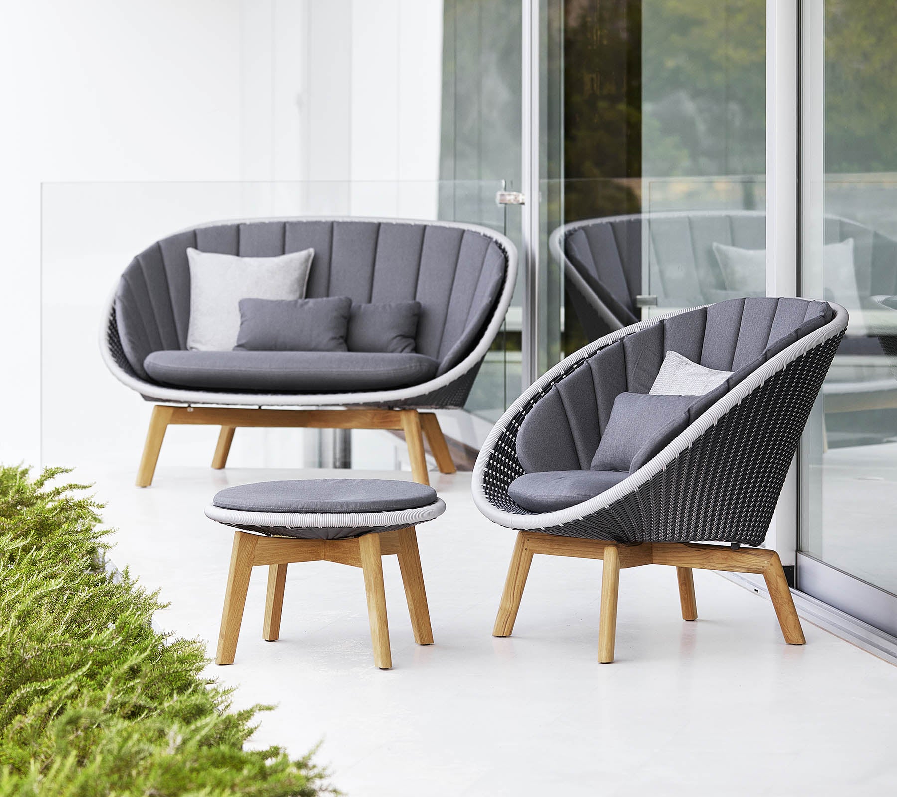 Stylisches Sitzset mit einem geschwungenen Sofa, Stuhl und runder Kaffeetisch, alle mit modernem Design und weichen grauen Kissen.