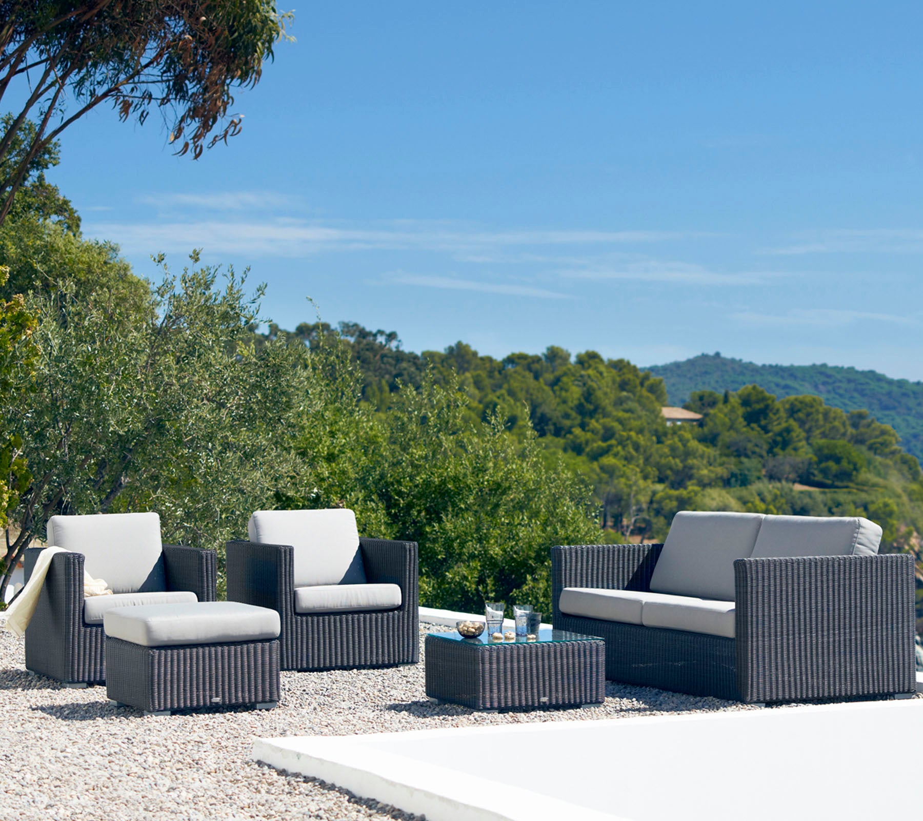 Stilvolle Gartensitzgruppe mit einem Sofa, zwei Sessel und einem Couchtisch mit einem schlanken Design und neutralen Kissen, umgeben von Grün.