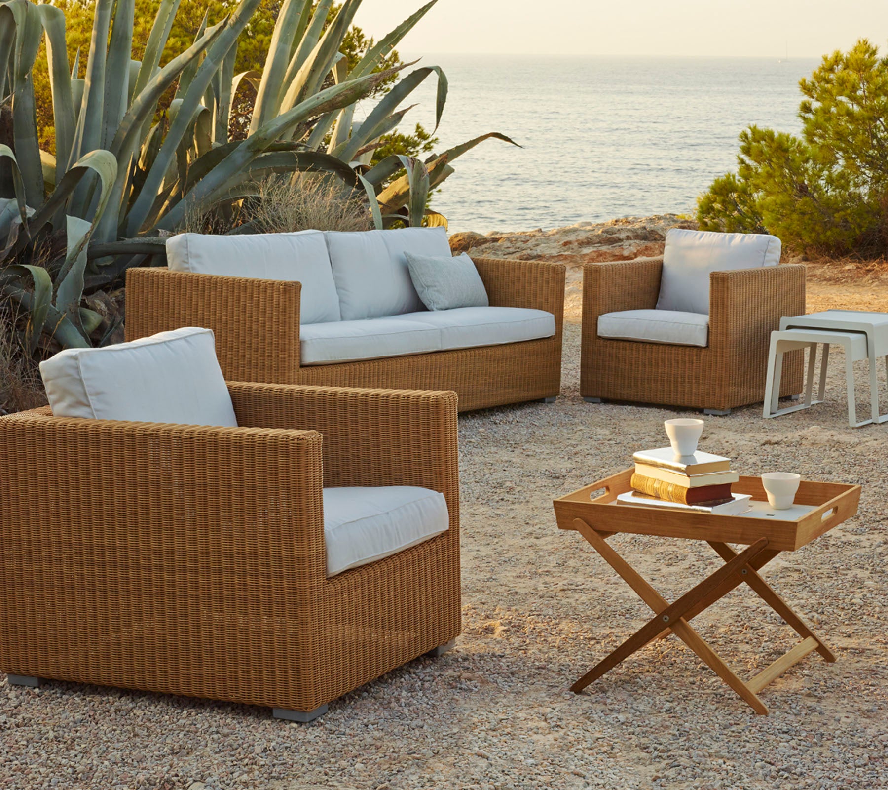 Stylisches Outdoor-Sitzarrangement mit geflochtenen Rattanstühlen und einem Sofa mit hellen Kissen, ergänzt durch einen Holztisch.