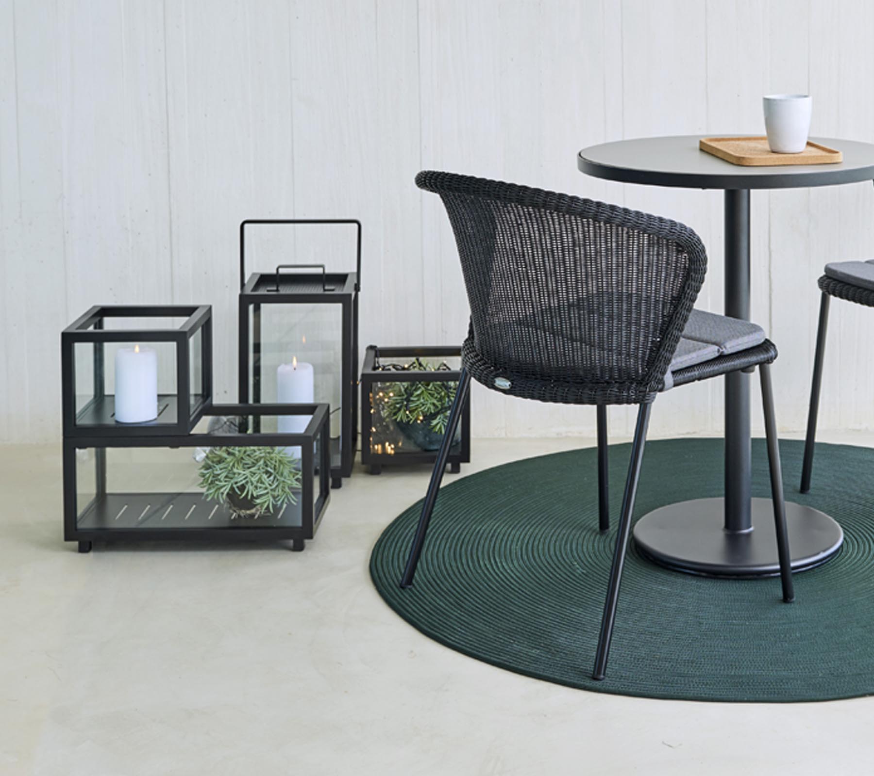 Moderne Sitzgelegenheiten und dekorative Glaslaternen mit Pflanzen, um einen runden Tisch herum angeordnet, auf einem runden grünen Teppich.