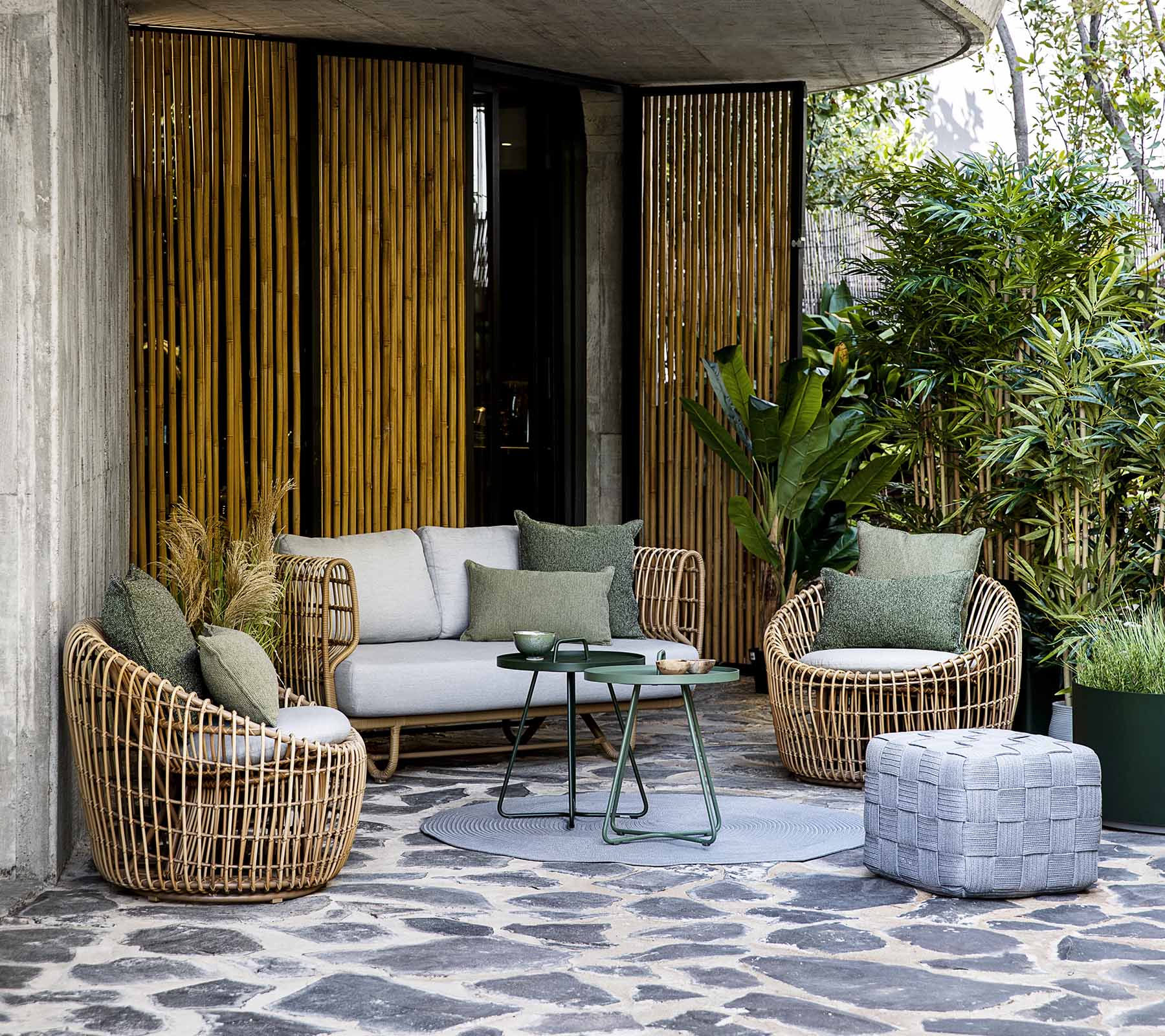 Stylischer Sitzbereich mit einem Sofa und runden Stühlen, ergänzt durch Kissen und einen Couchtisch, umgeben von Grünpflanzen.