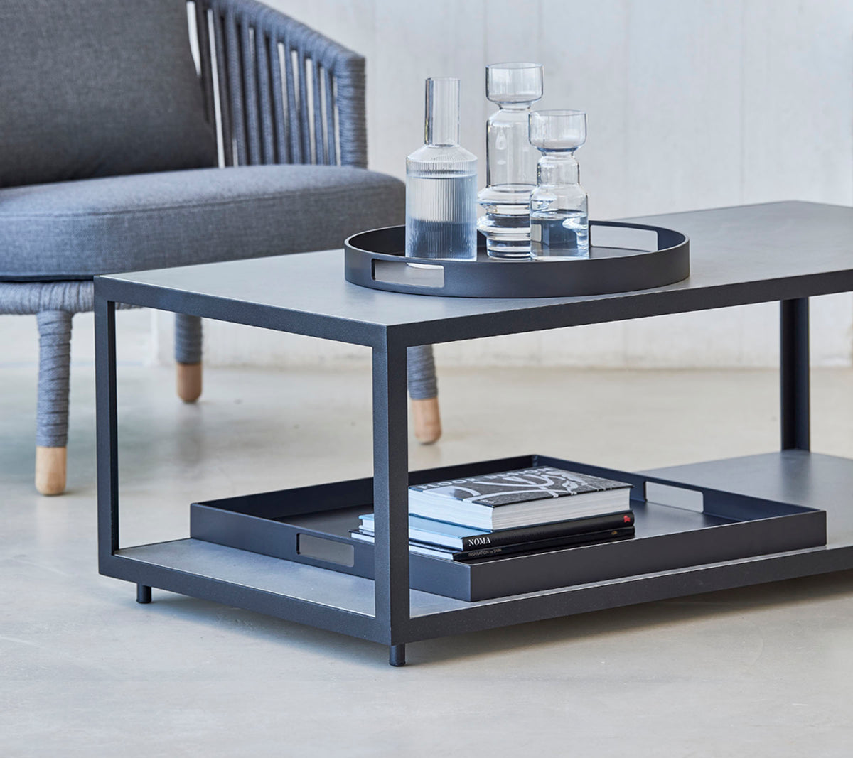 Modernes Couchtisch mit einem schlanken Design, mit einem Tablett, Gläsern und Büchern auf dem unteren Regal. Ideal für stilvolle Wohnräume.