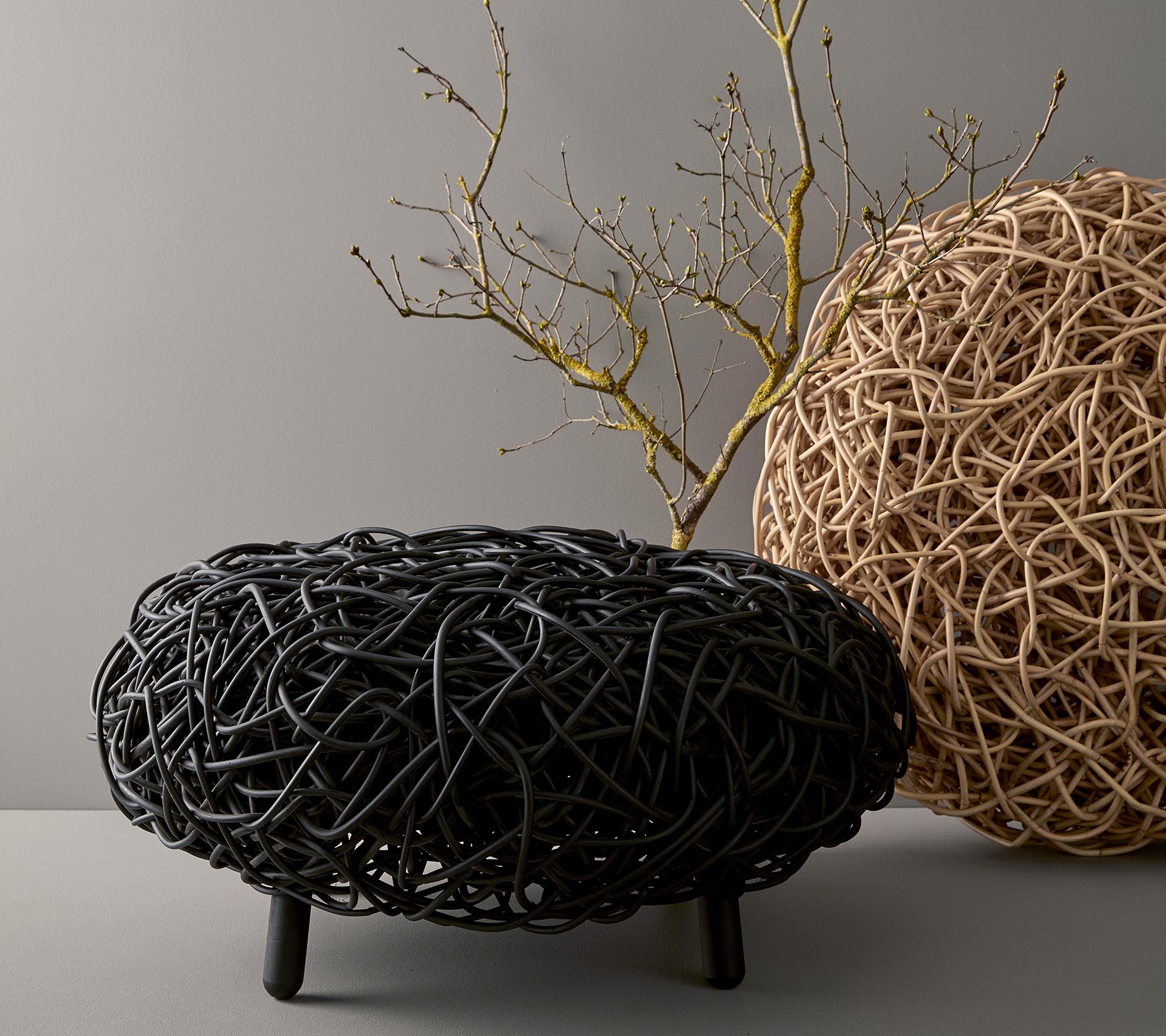 Ein stilvoller, runder Couchtisch aus gewebtem Material, der schwarze und natürliche Töne zeigt, mit einem dekorativen Ast oben drauf.