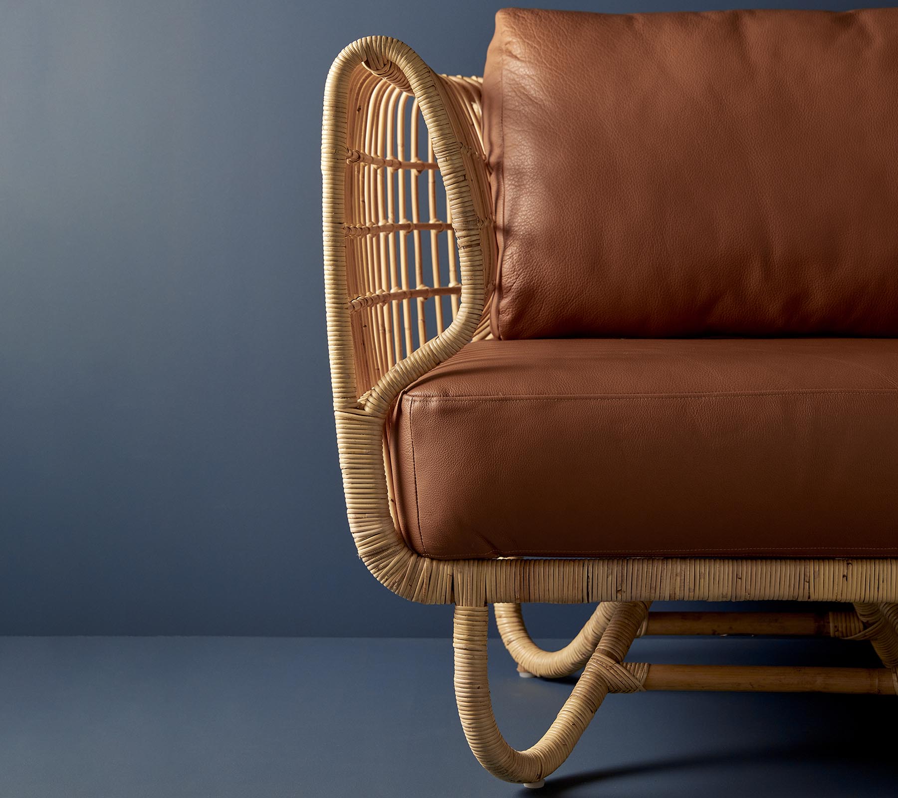 Rattanstuhl mit einer gewölbten Form und braunen Lederkissen, der eine Mischung aus natürlichen Materialien und modernem Design präsentiert.