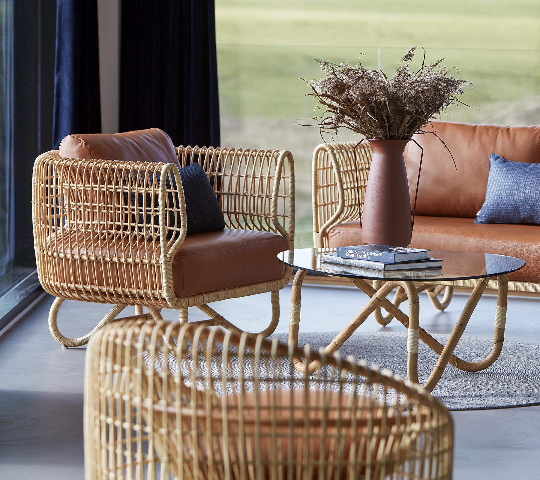 Stilvolle Sitzgelegenheiten mit geflochtenen Rattanrahmen, Lederkissen, einem eleganten Couchtisch und einer Vase mit getrocknetem Laub, die eine gemütliche Atmosphäre schaffen.