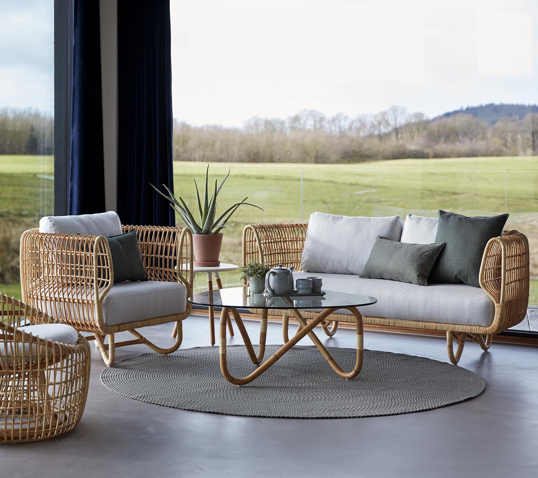 Eine stilvolle Sitzgelegenheit mit geflochtenen Möbeln, einem runden Teppich und einem Glastisch, ergänzt durch minimalistische Dekorelemente.