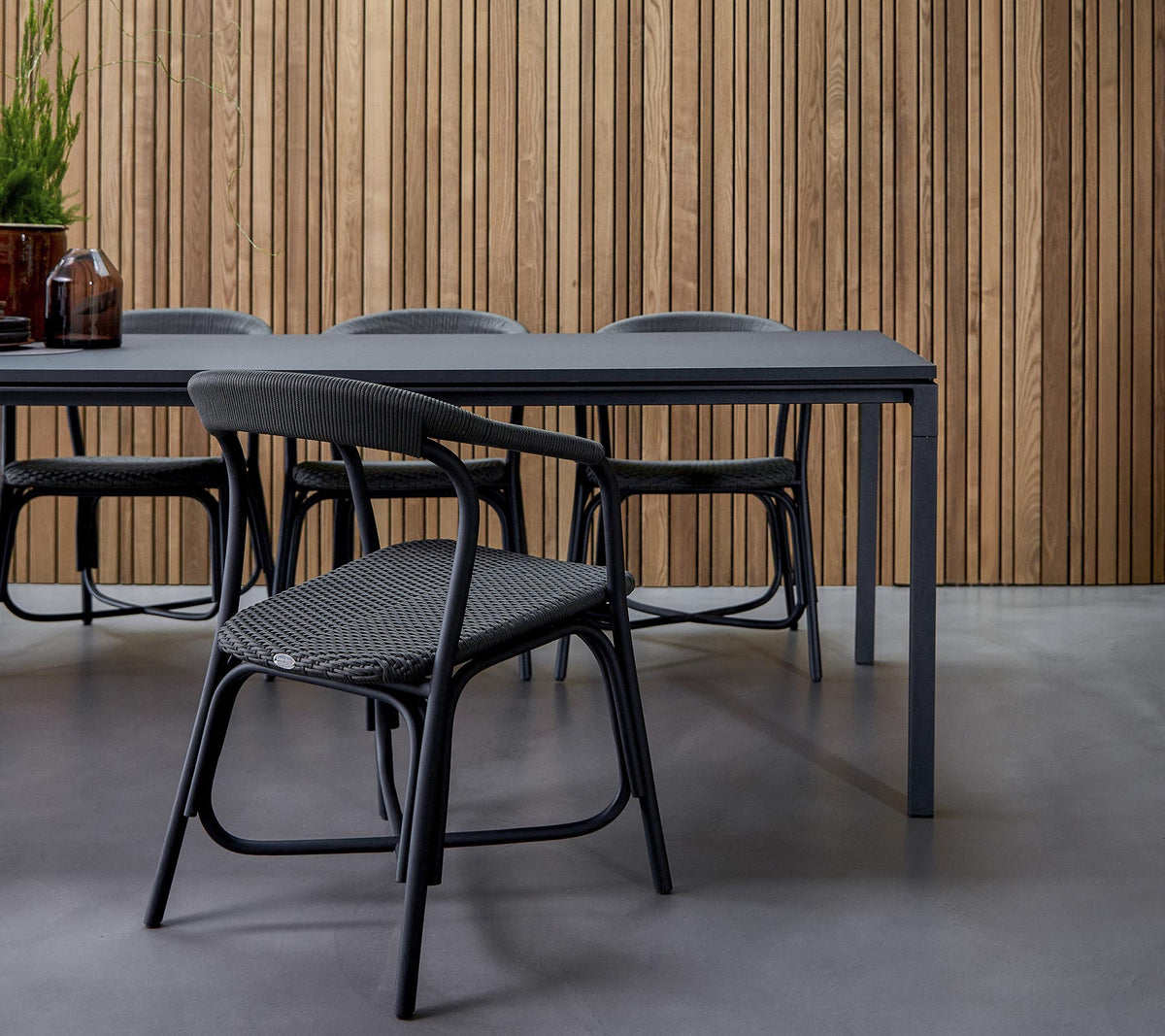 Ein modernes Essbereich mit einem eleganten Tisch, umgeben von stilvollen Stühlen, vor einem strukturierten Holz-Hintergrund.