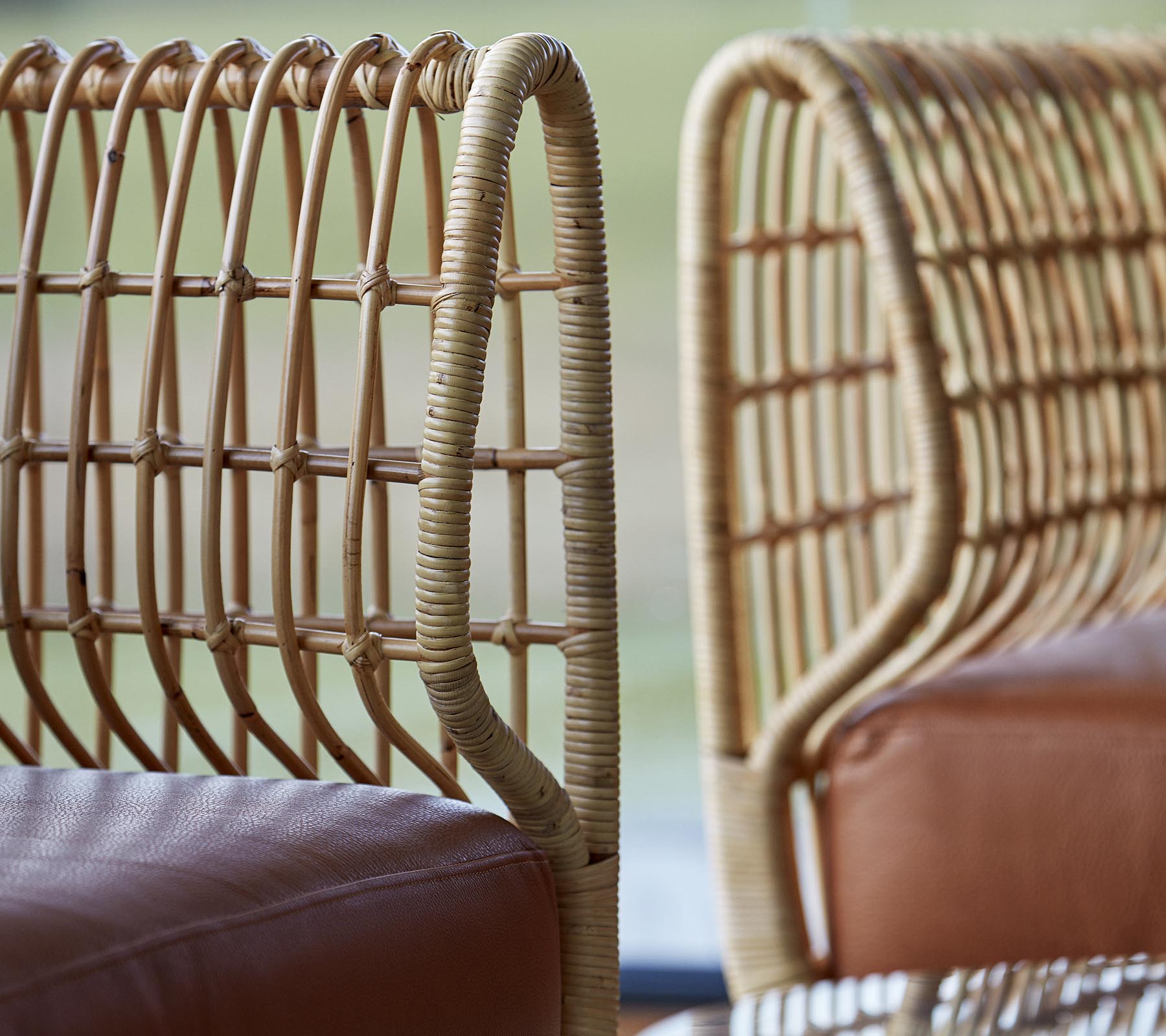 Zwei stilvolle Stühle mit geflochtenen Rattansitzen und glatten Lederpolstern, die eine moderne Designästhetik präsentieren.