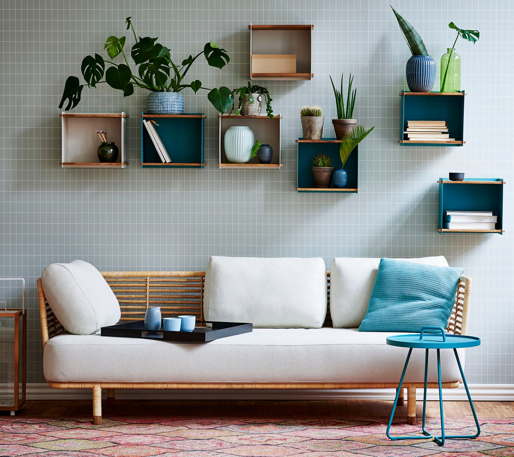 Ein stilvolles Sofa mit einem leichten Kissen und einem kleinen Tisch, geschmückt mit verschiedenen Topfpflanzen, die auf geometrischen Regalen präsentiert werden.