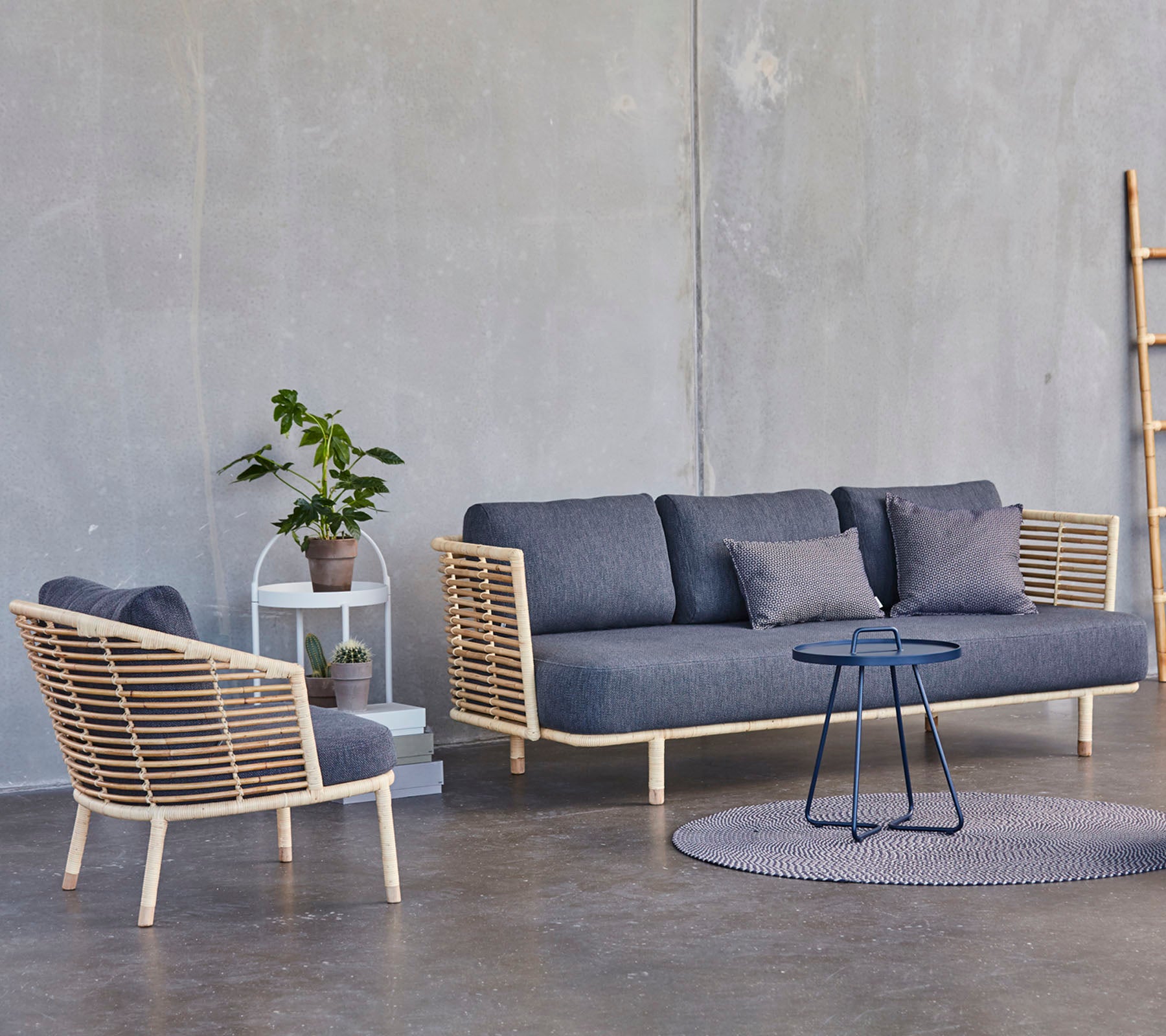 Eine moderne Sitzanordnung mit einem stilvollen Sofa und Sessel mit Holzakzenten, begleitet von einem kleinen Beistelltisch und einer Topfpflanze.