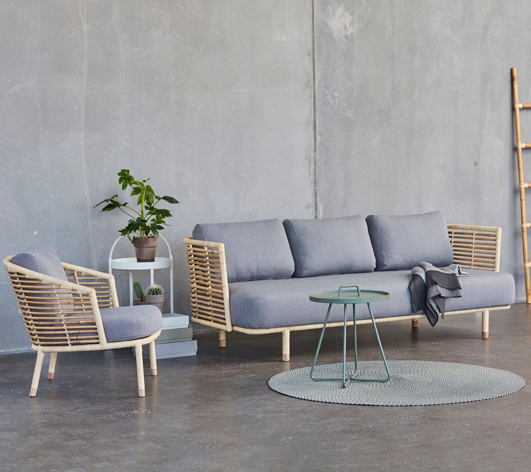 Eine moderne Sitzgelegenheit mit einem grauen Sofa, einem passenden Stuhl, einem runden Teppich und einem kleinen Tisch mit einer Topfpflanze.