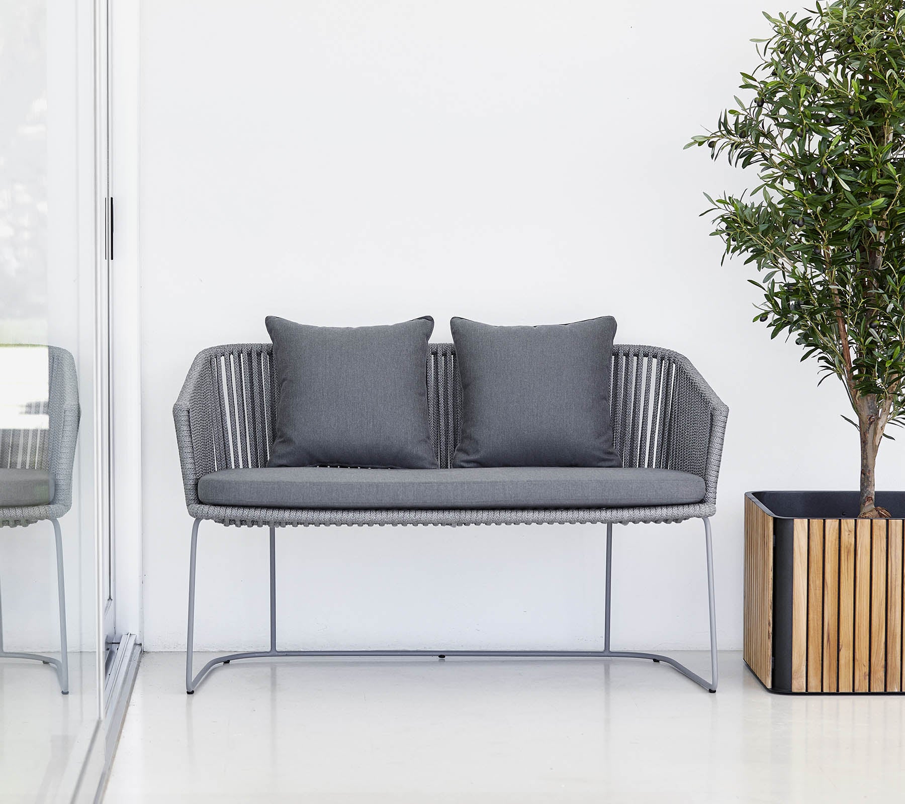 Ein modernes graues Zweisitzer-Sofa mit Kissen, begleitet von einer Topfpflanze und einem Holzpflanzgefäß.