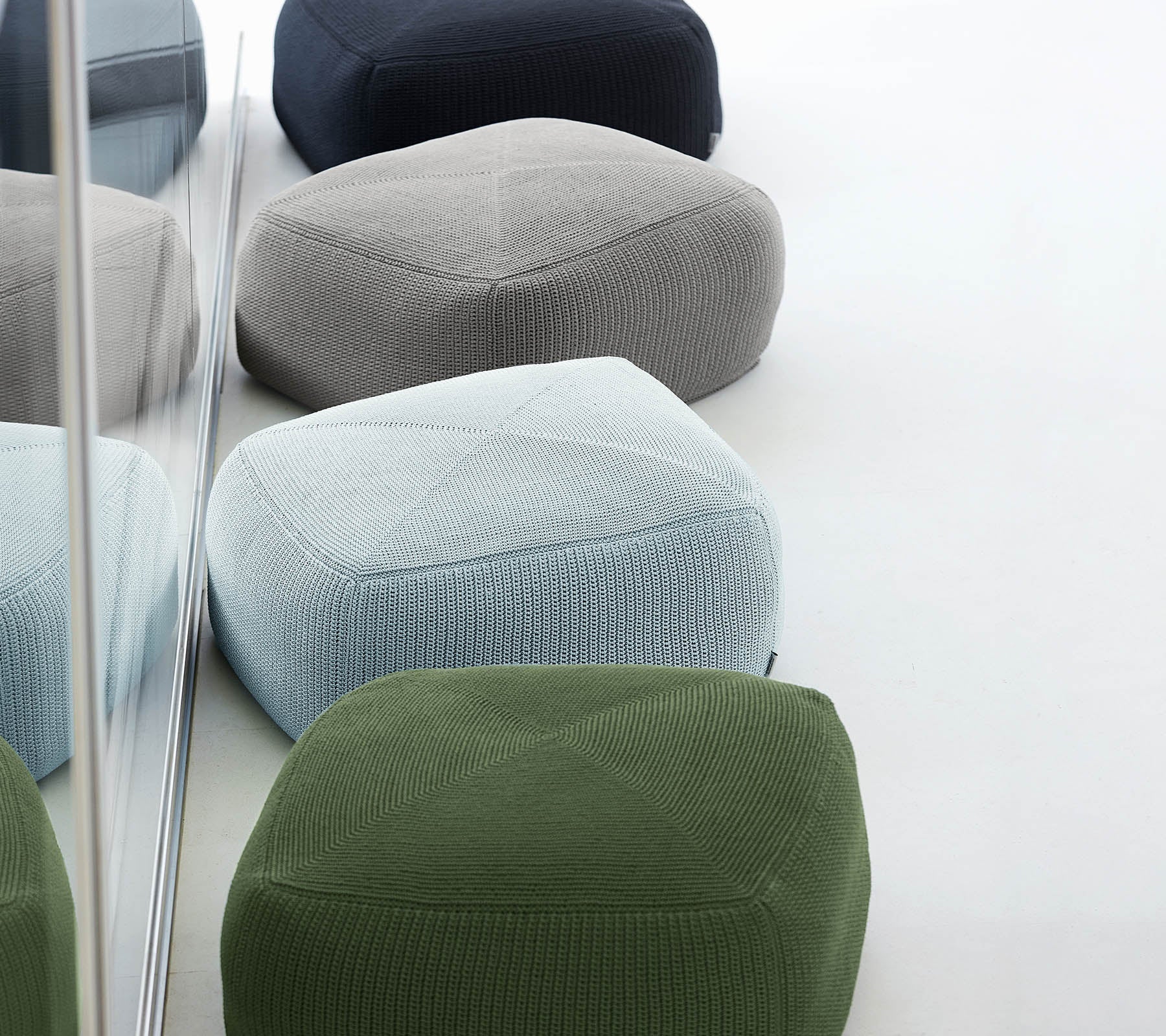 Eine Sammlung von bunten, strukturierten Poufs in verschiedenen Farbtönen, die zusammen angeordnet sind und stilvolles und modernes Design widerspiegeln.