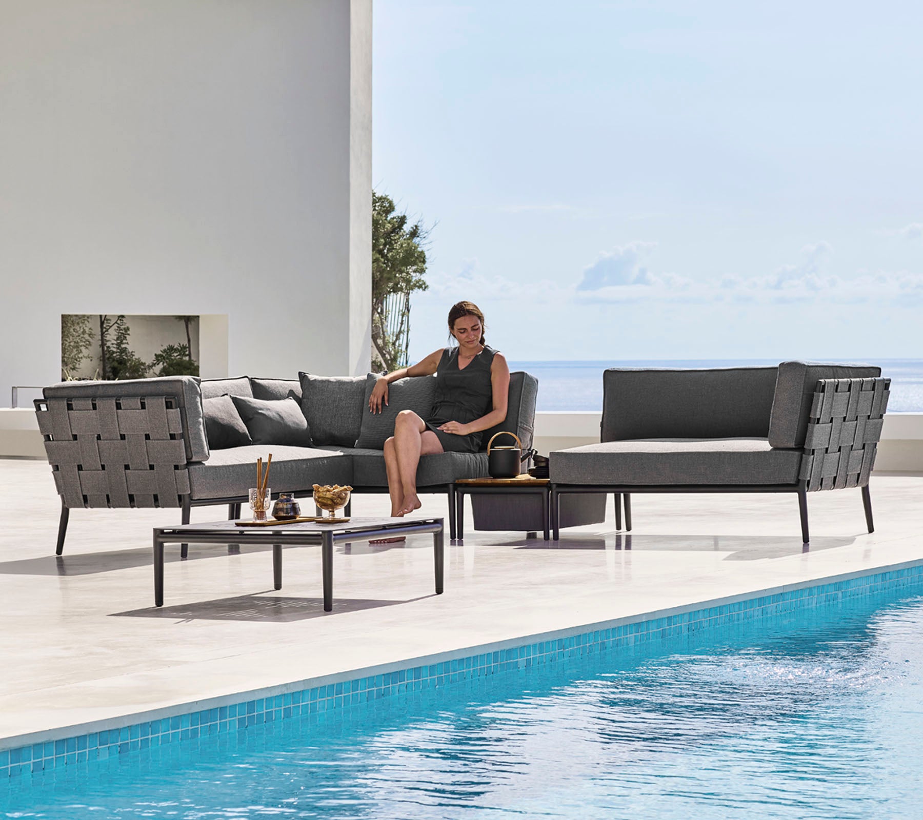 Ein stylisches Outdoor-Loungeset mit eleganten Sitzplätzen und einem Glastisch neben einem Pool, während eine Person bequem entspannt.